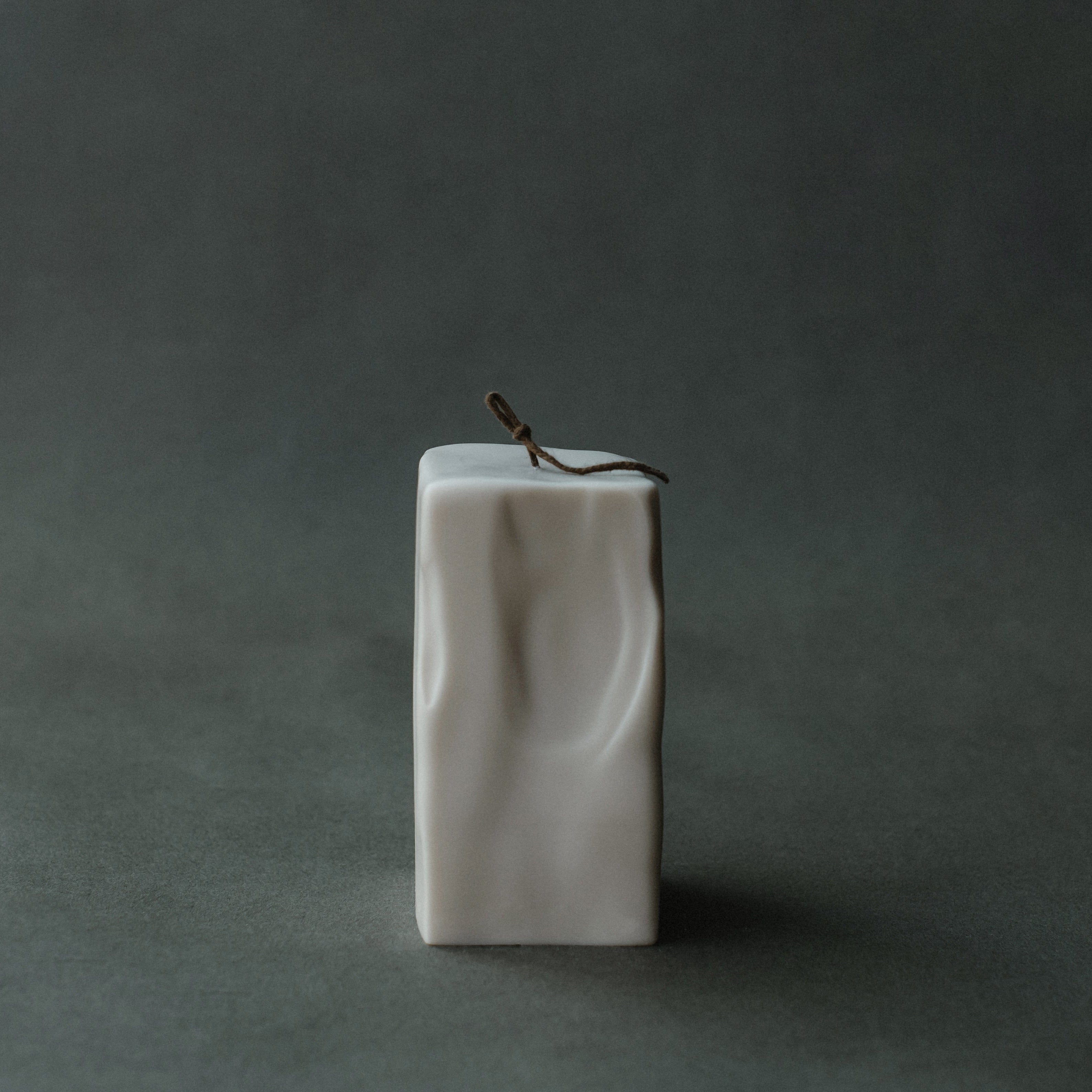 Large raw block pillar candle by LAWA with textured surface on a dark green background