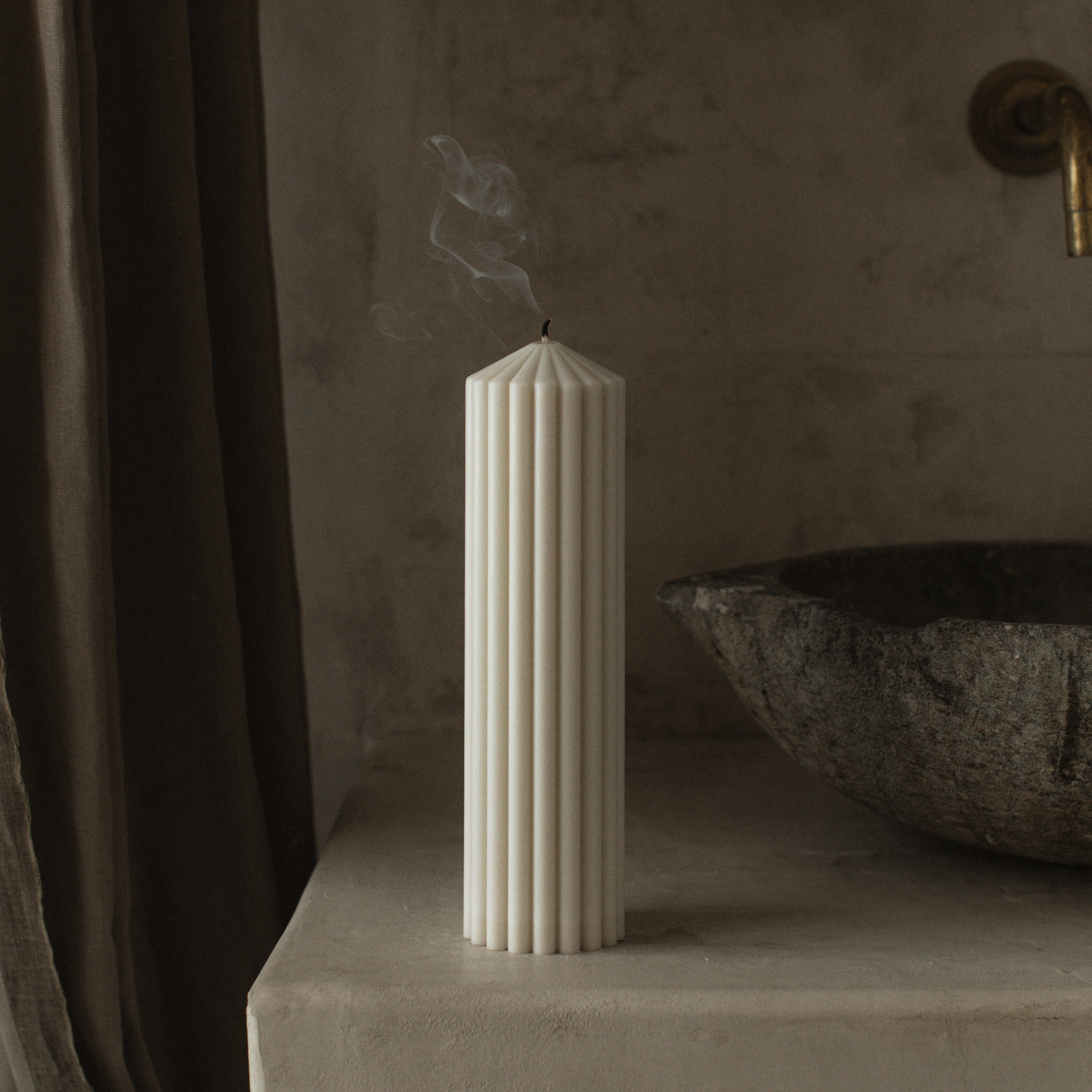 Minimalist large white peak pillar candle by LAWA with clean mountain-inspired design on a stone surface next to a textured wall and dark curtain.