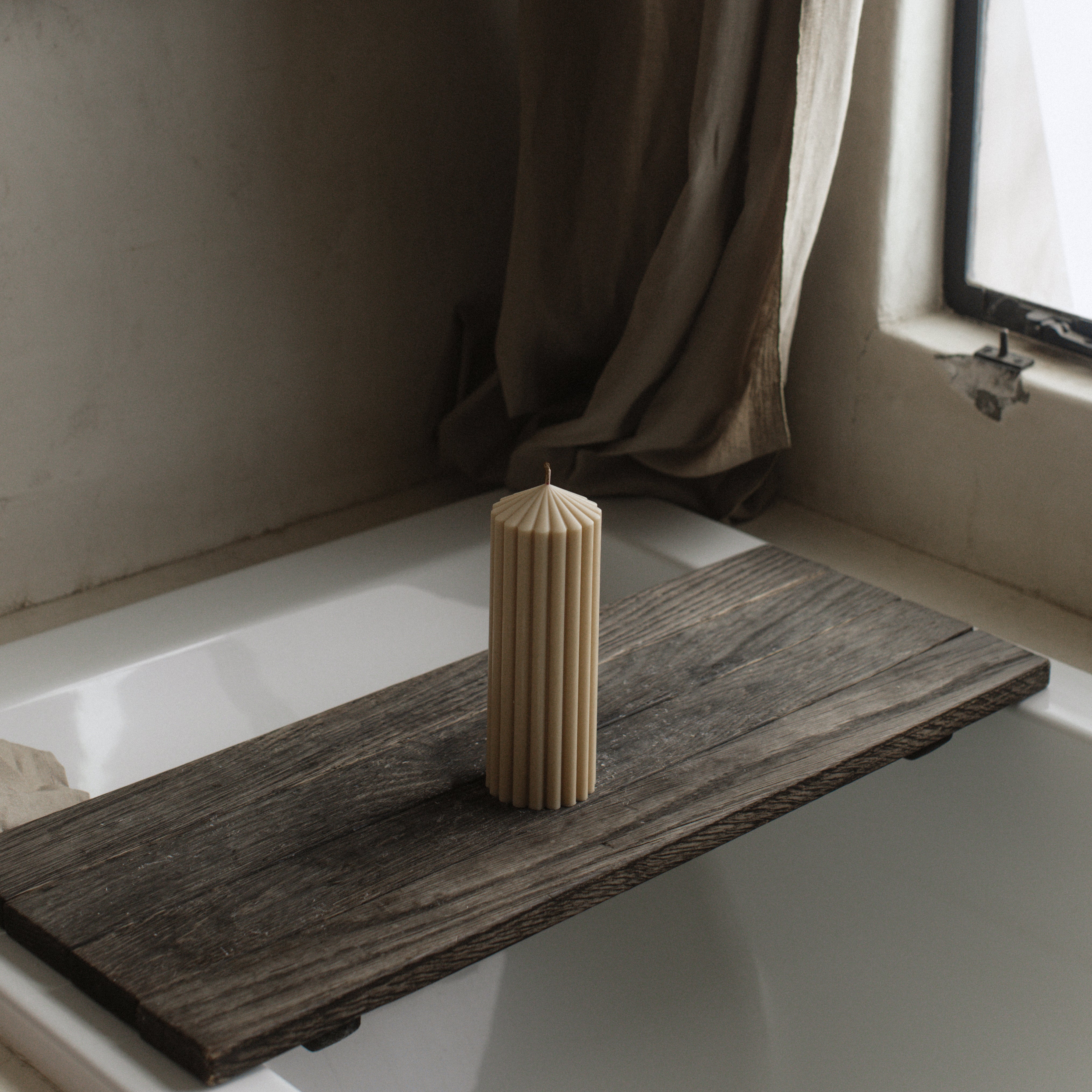 LAWA medium sandstone soy wax peak candle featuring a modern geometric silhouette on a Wooden bathtub tray with a cylindrical beige candle on a white bathtub.