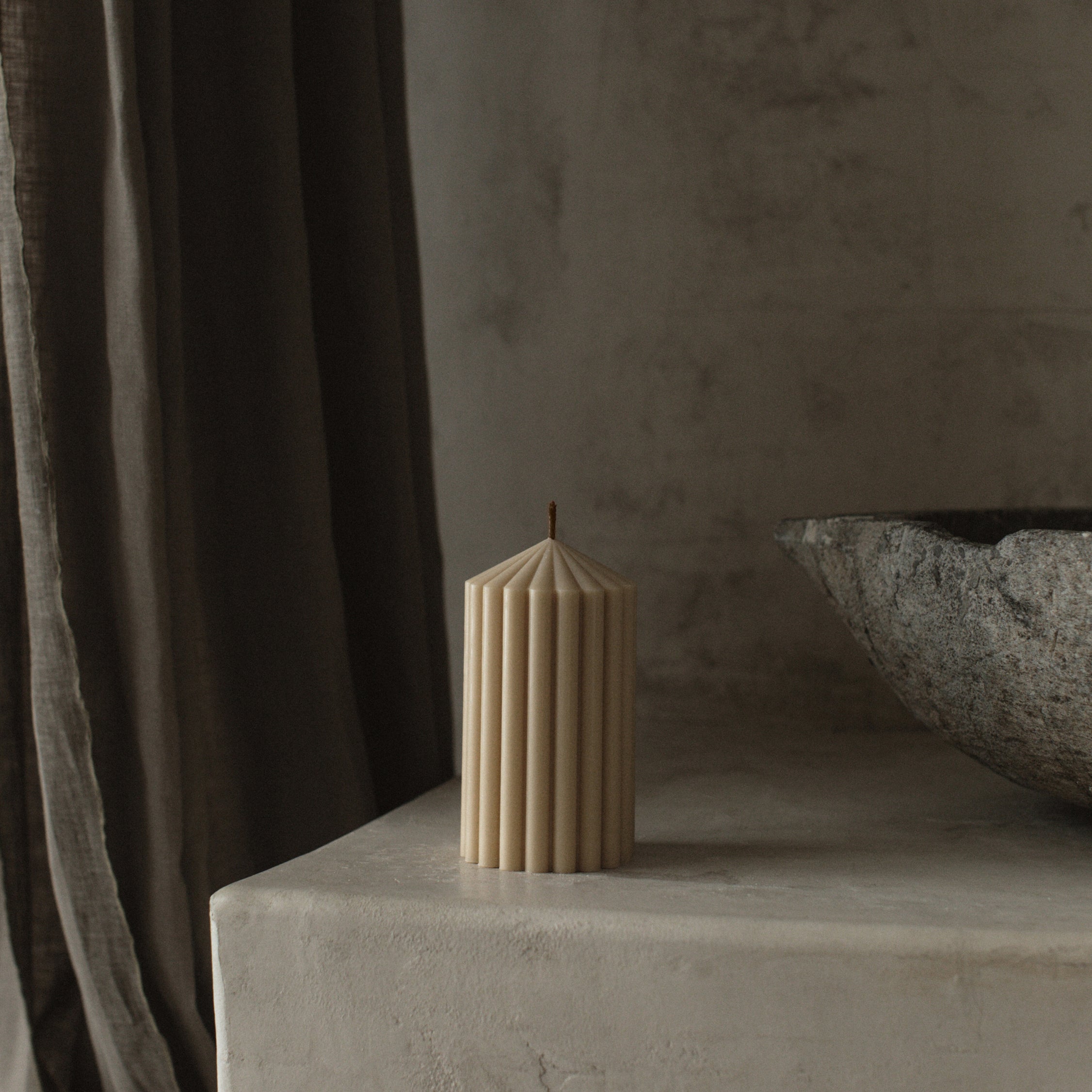 Minimalist small sandstone peak candle by LAWA featuring a clean mountain-inspired shape on a stone surface with a textured wall and curtain in the background
