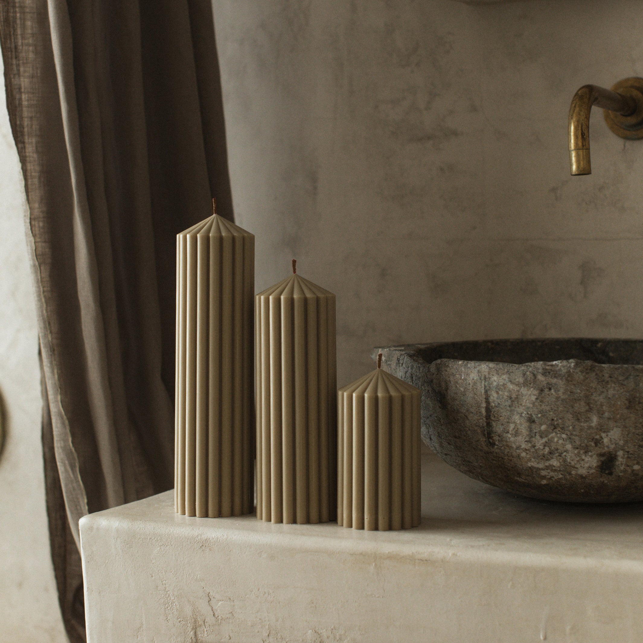 Olive beige soy wax peak pillar candle set of 3 three by LAWA with geometric minimalist design on a stone surface with a stone bowl and faucet in the background.