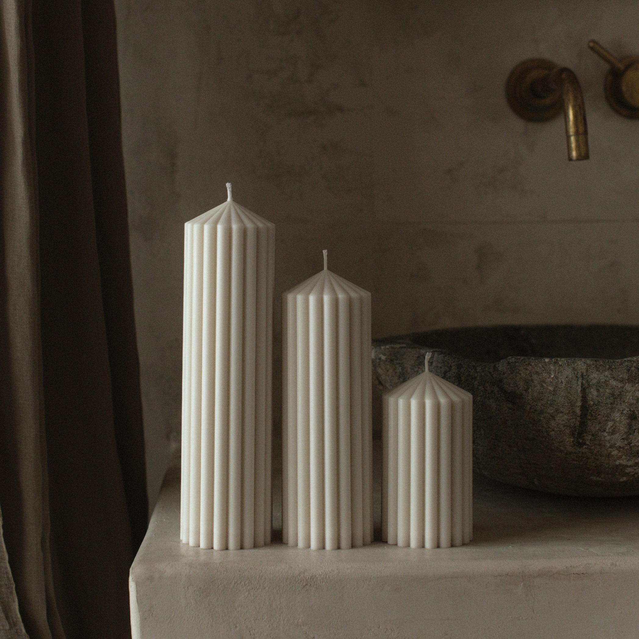White soy wax peak pillar candle set of 3 by LAWA with minimalist geometric silhouettes on a stone surface with a rustic bathroom background