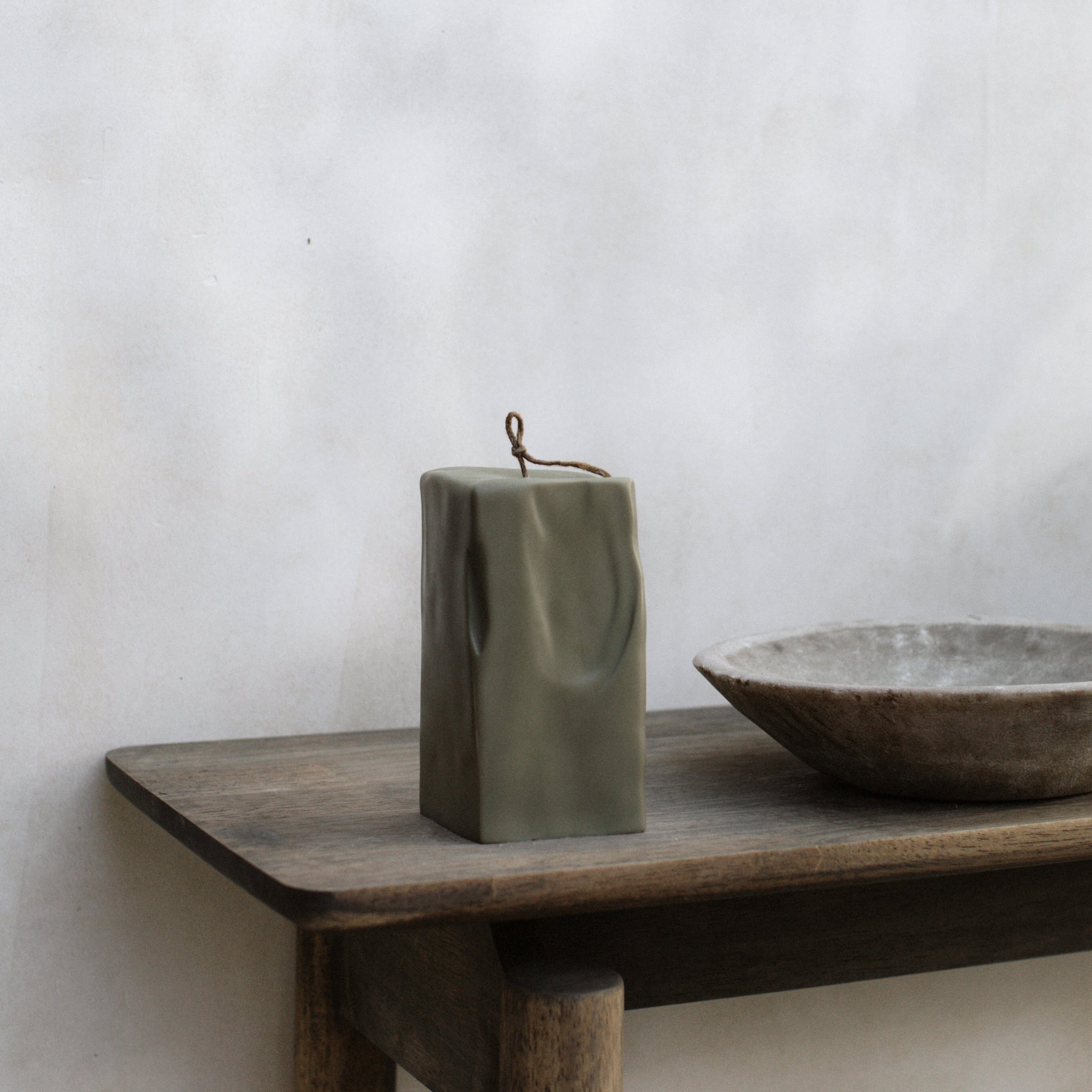 Modern large earthy green raw block pillar candle by LAWA on a wooden table against a white wall.