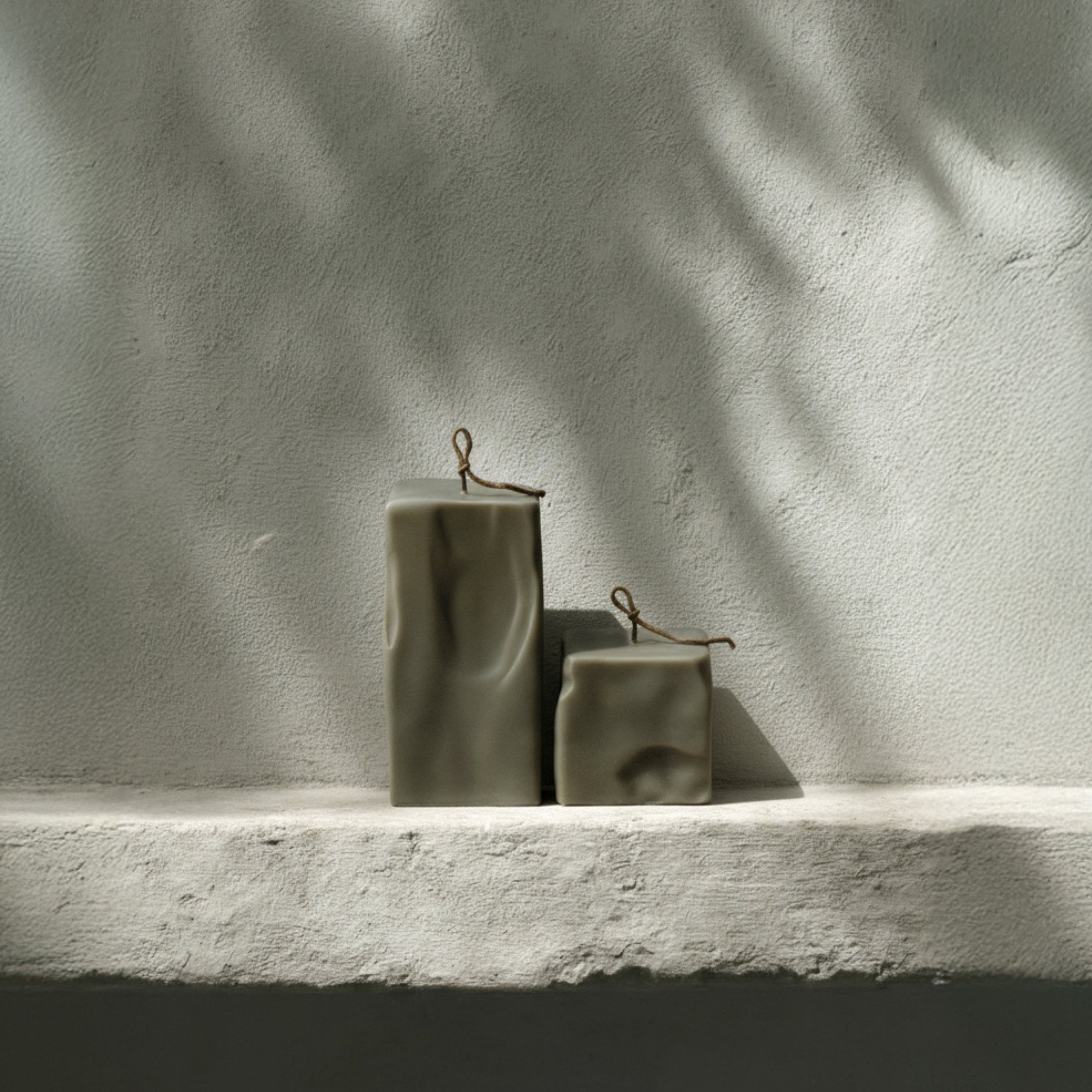 Earthy green raw block candle duo by LAWA on a ledge with a textured wall background