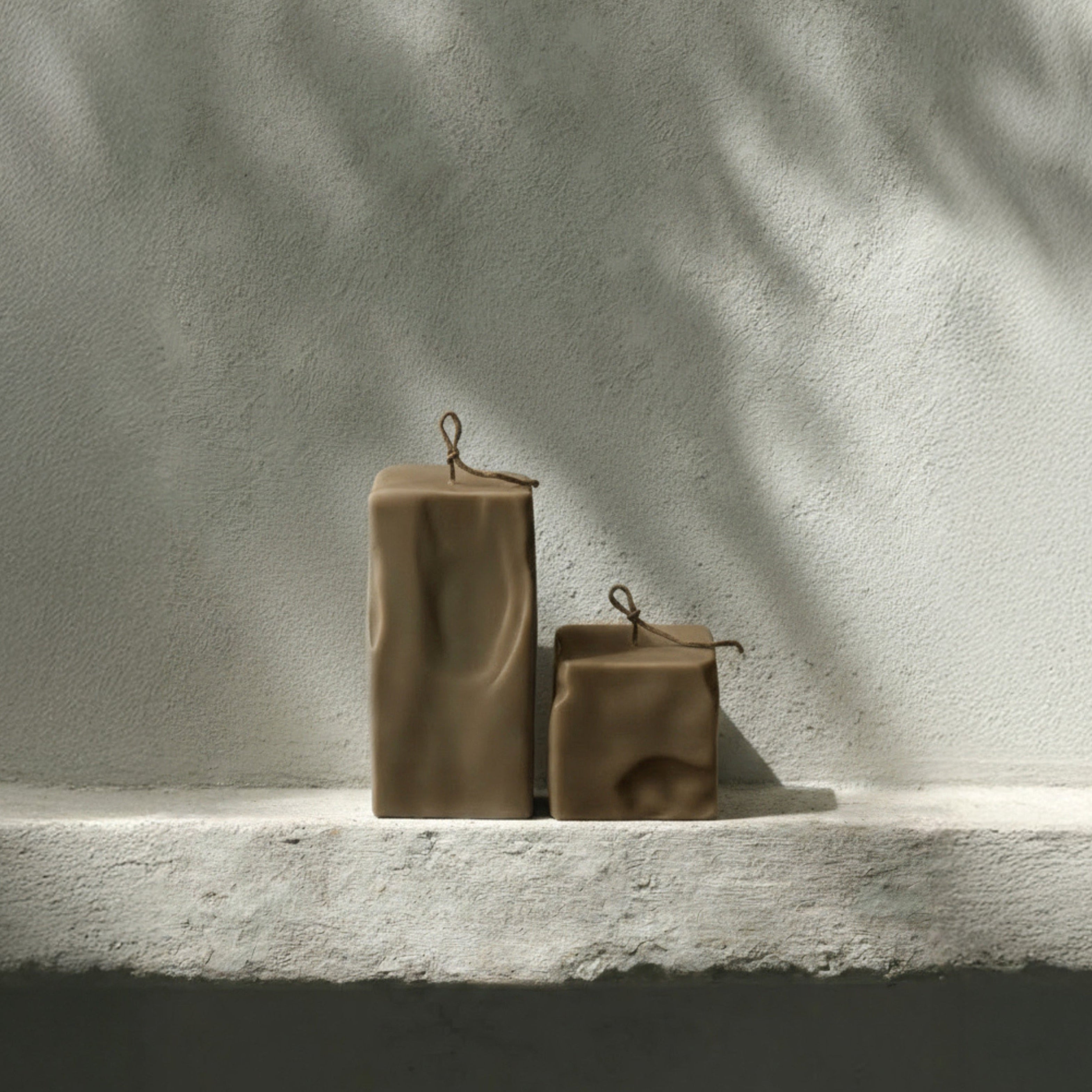 Set of two kobicha raw block candles by LAWA on a light stone surface with a textured wall background.