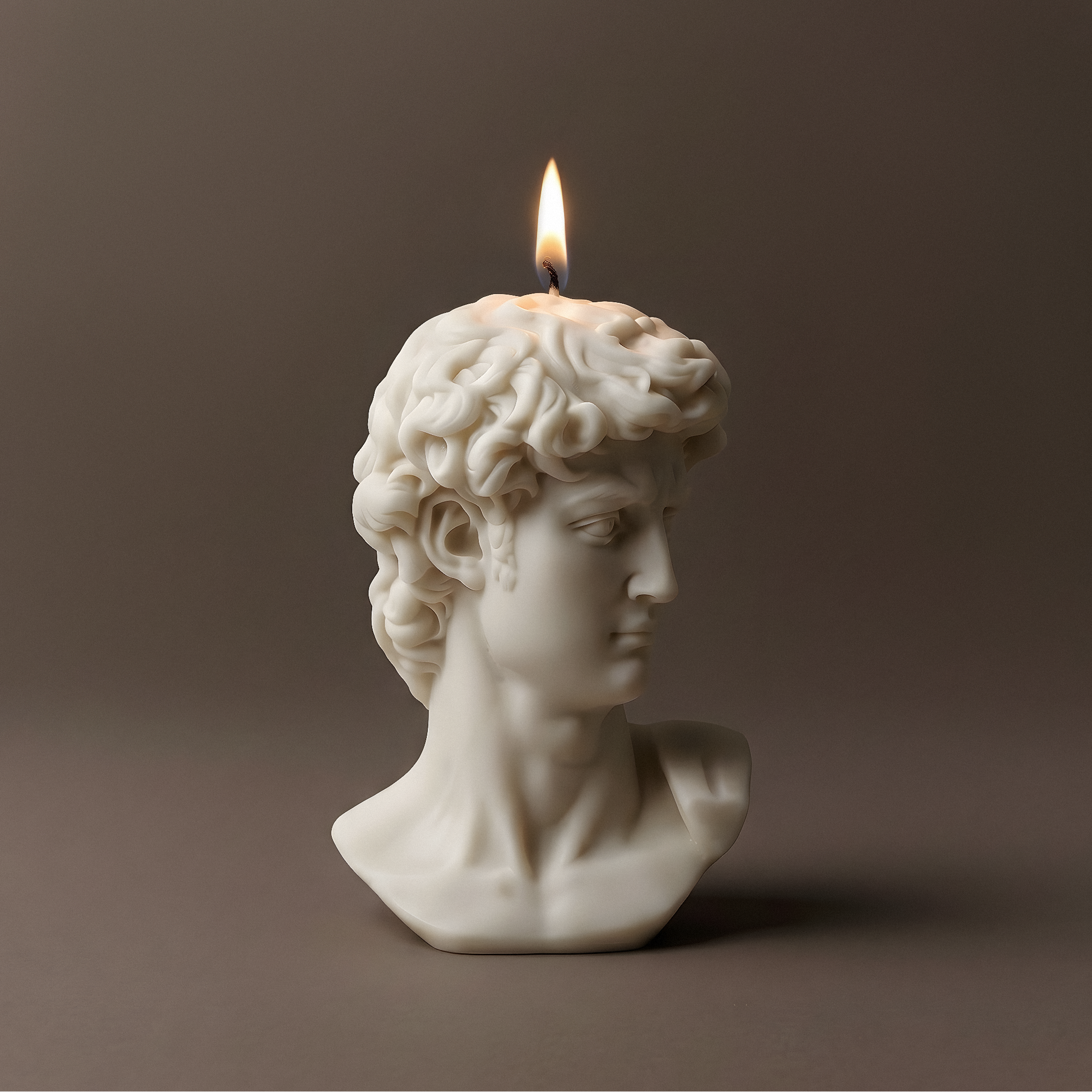 Candle shaped like a classical bust with a lit flame on a dark background