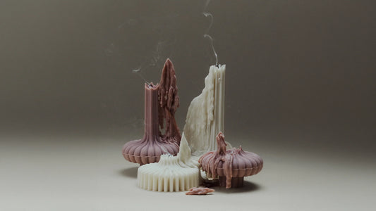 Handmade sculptural pillar candles in dusty rose and cream with melted wax drips and wisps of smoke after being blown out