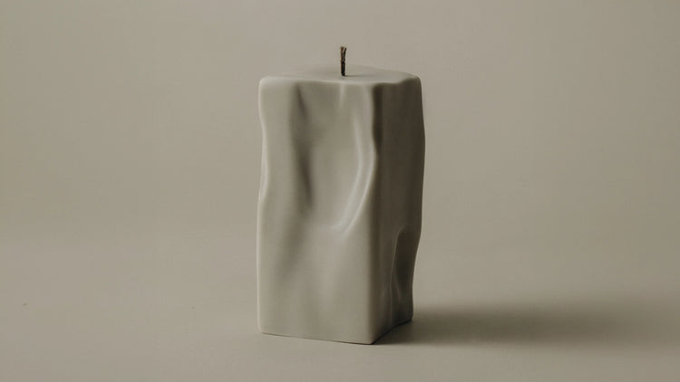 A raw sculptural pillar candle in off-white with an organic rippled surface, on a neutral background.