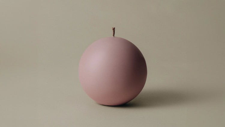 A round sphere candle in dusty rose with a single wick, shown against a neutral background.