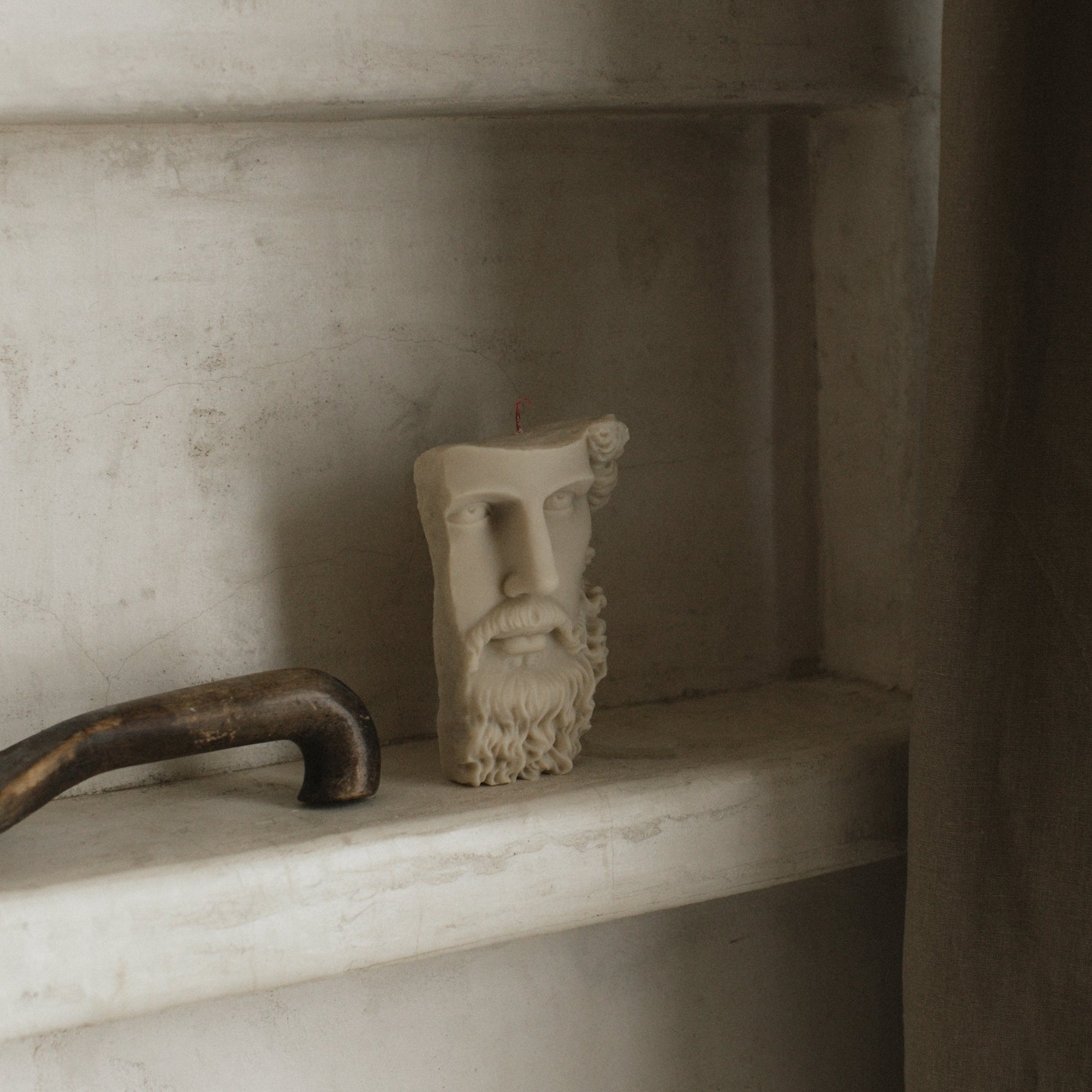 A handmade soy wax candle with a geometric form, displaying an abstract face design, placed on a shelf.