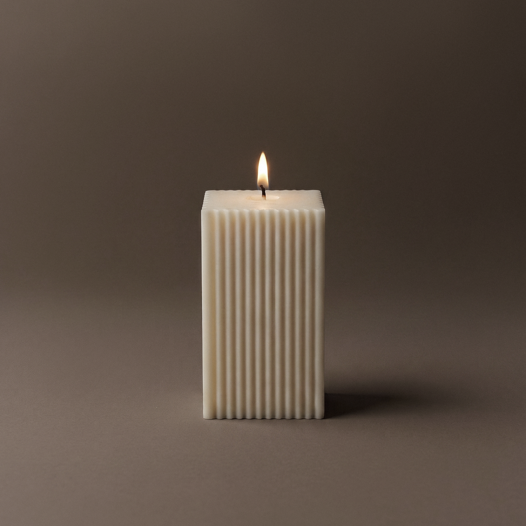 Rectangular white candle with a flame on a dark brown background