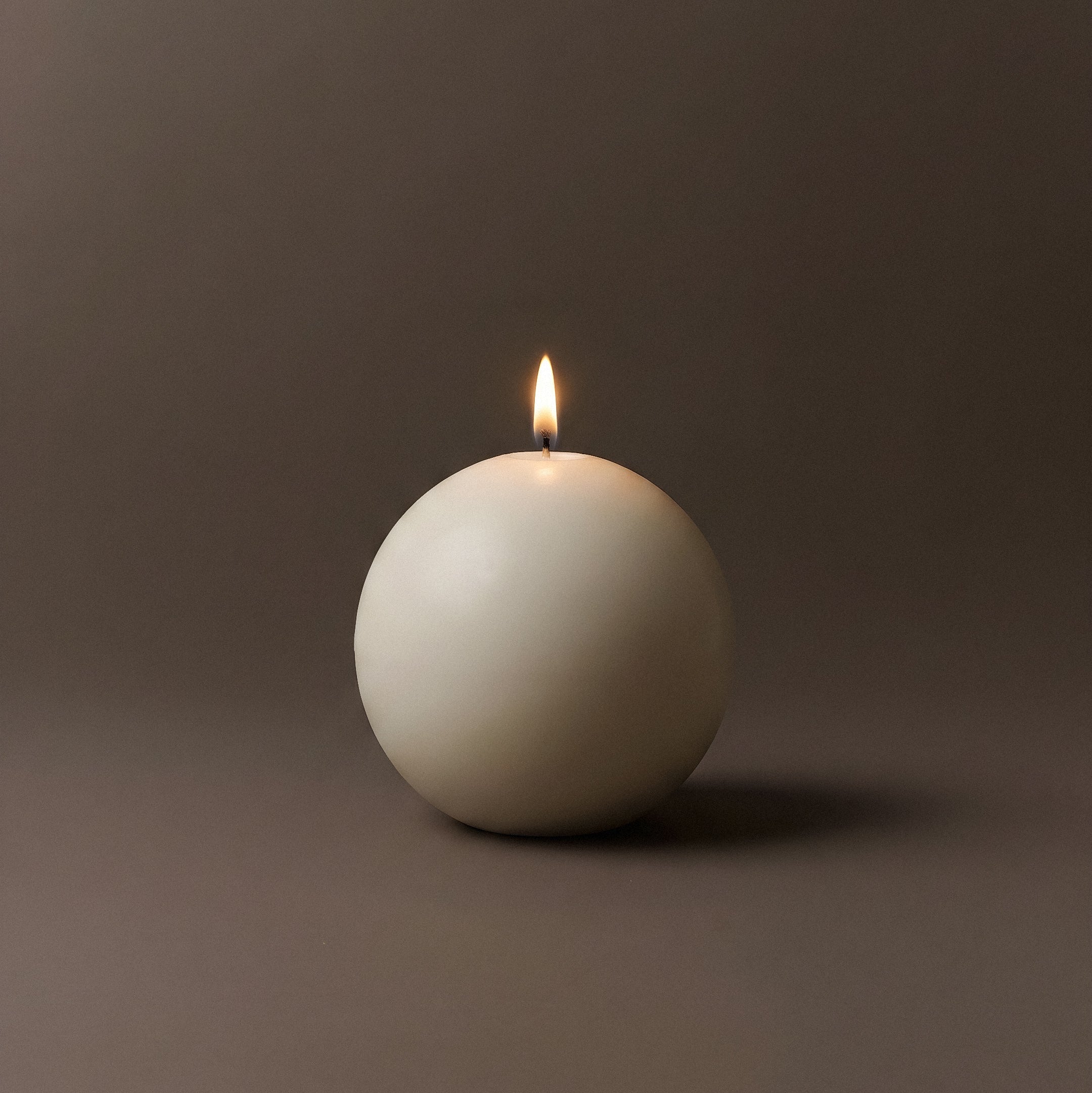 Spherical white candle with a lit wick on a dark background