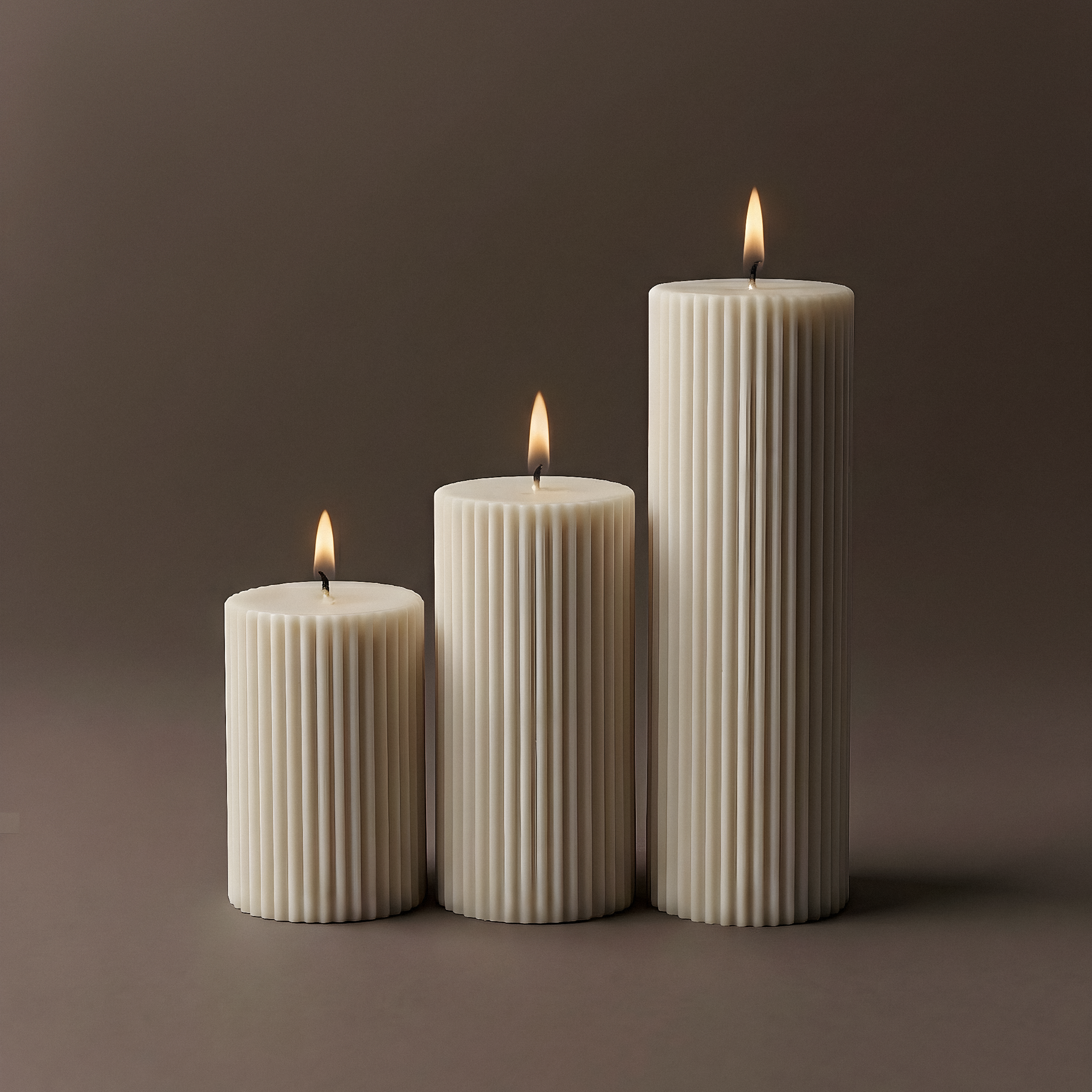 Three ribbed candles of different sizes on a brown background