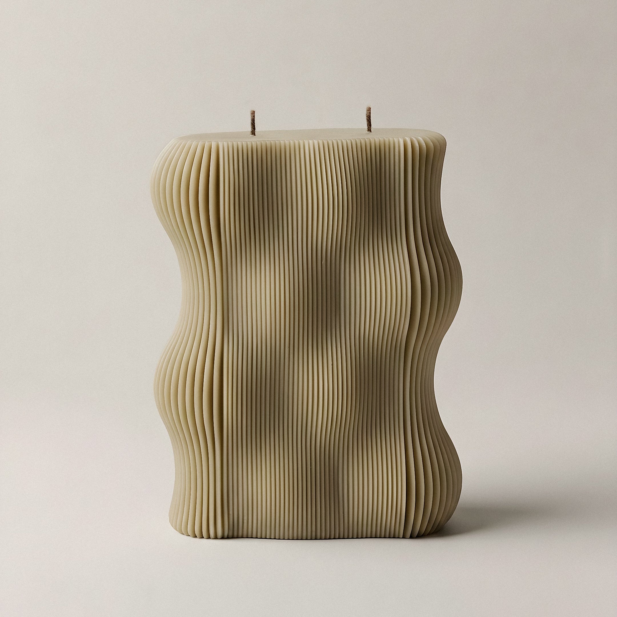 Handmade wavy sculptural candle detail showing smooth soy wax curves and organic flowing form on neutral surface