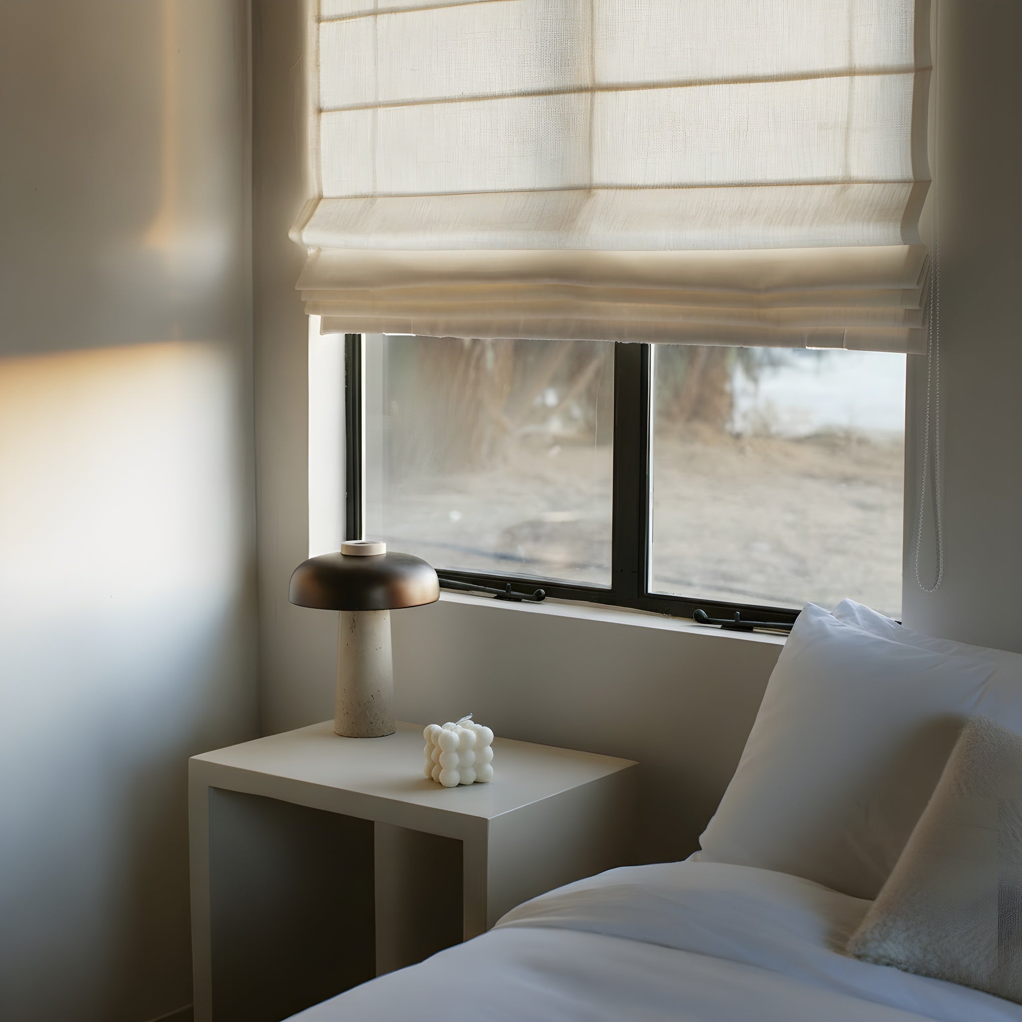 Minimal white bubble candle by LAWA with modern sculptural stacked bubble shape for a Modern bedroom with a bed, nightstand, and window with light filtering through.