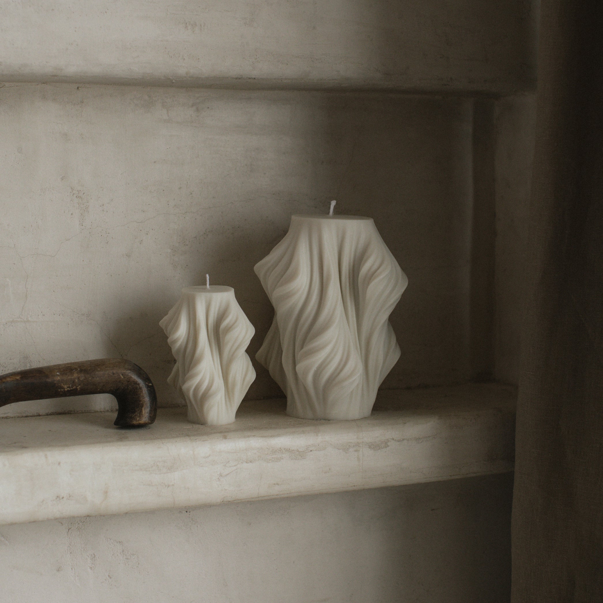 Two textured cascading pillar  candles on a stone shelf with a neutral background
