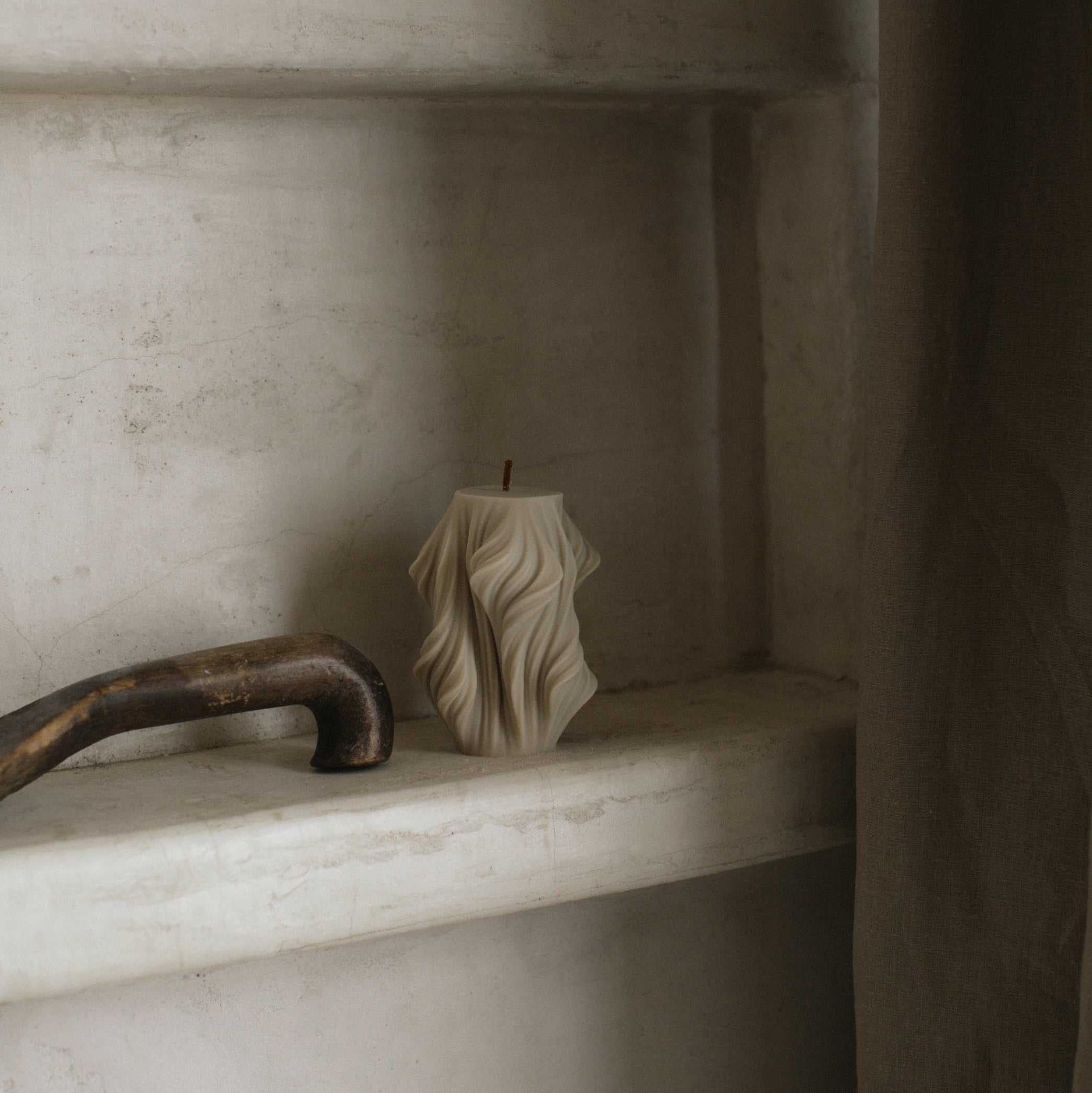 Decorative cascading pillar candle on a marble shelf with a rustic handle.