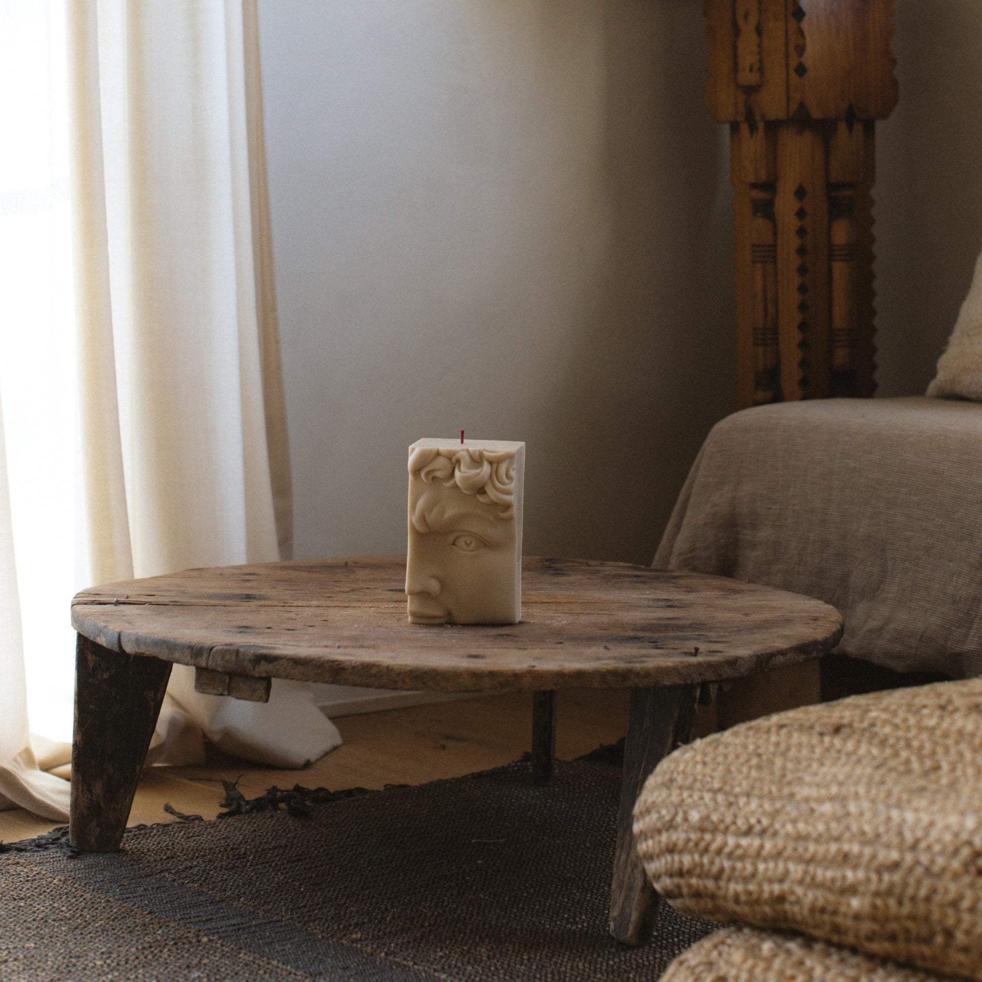 David Half Face soy wax pillar candle in a Living room with a wooden coffee table, candle, and textured sofa.