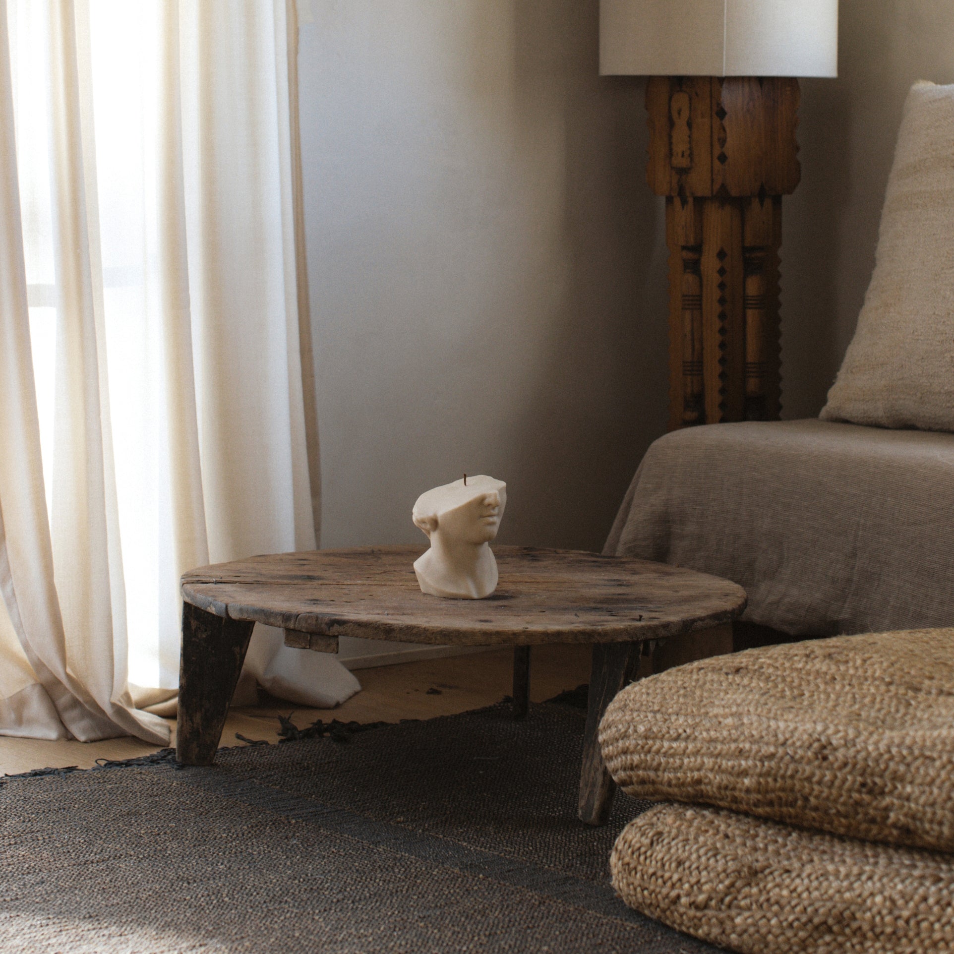 Moon gray classical Greek statue pillar candle by LAWA with detailed sculpted form for a Living room with wooden table, sculpture, and armchair.