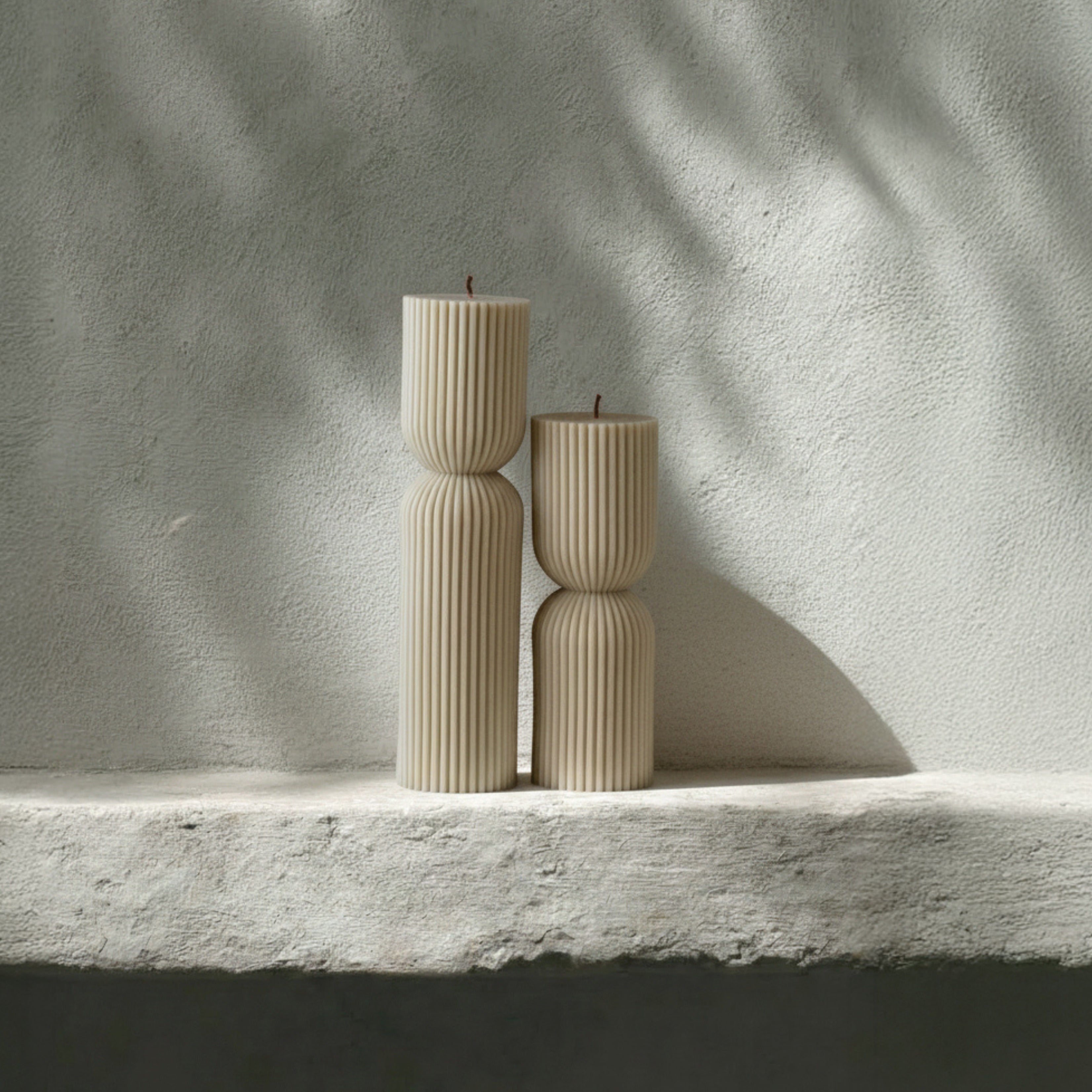 Hourglass set of two candles on a stone surface with a light gray background
