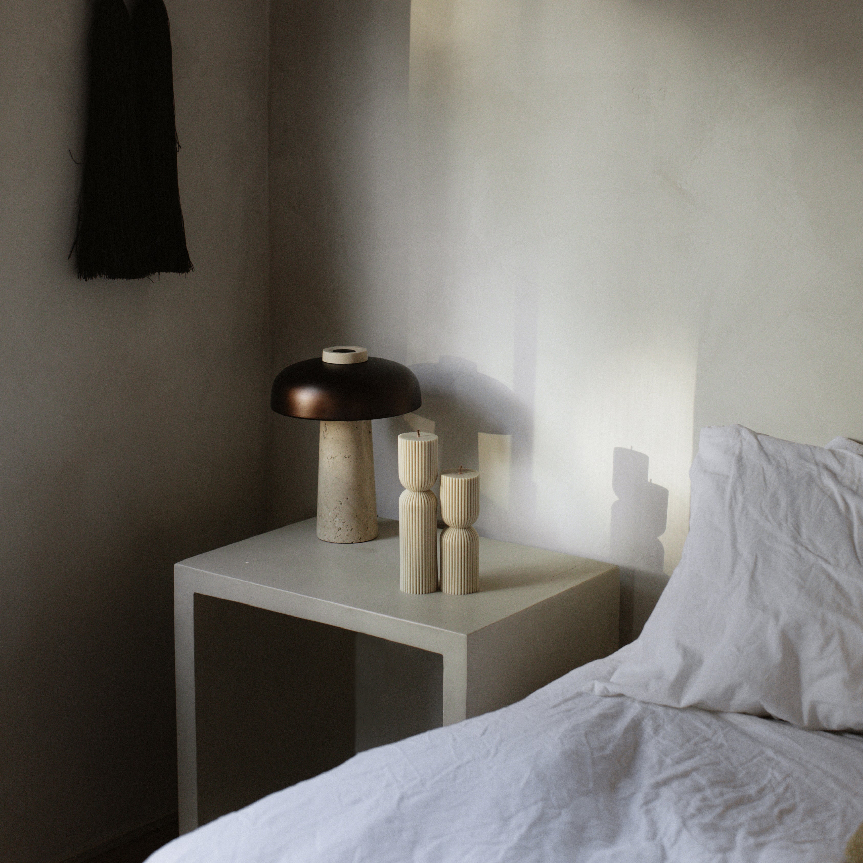 Modern bedroom with a bedside table featuring a lamp and a decorative hourglass set of two pillar candles.