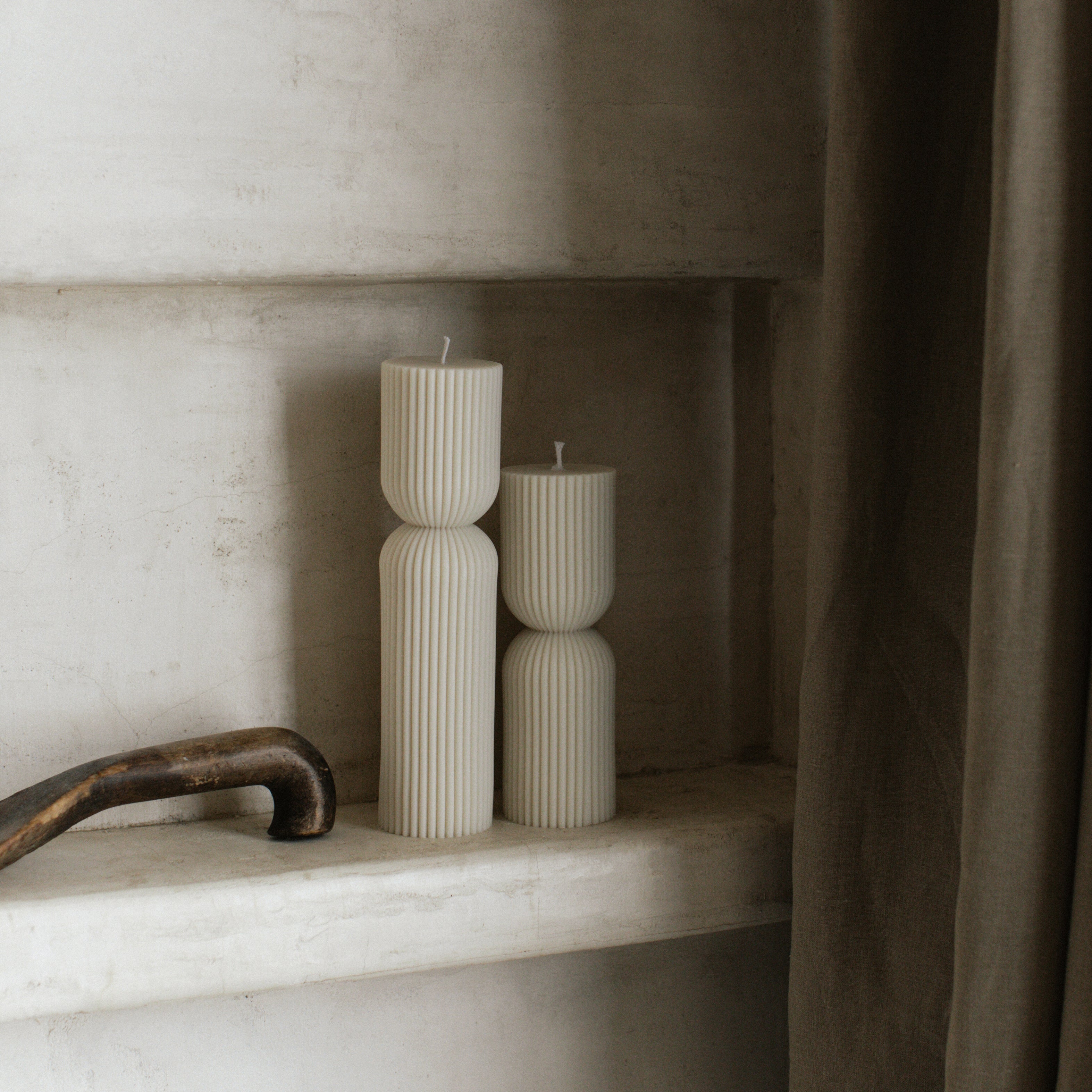 White hourglass set of two pillar candles on a shelf with a neutral background