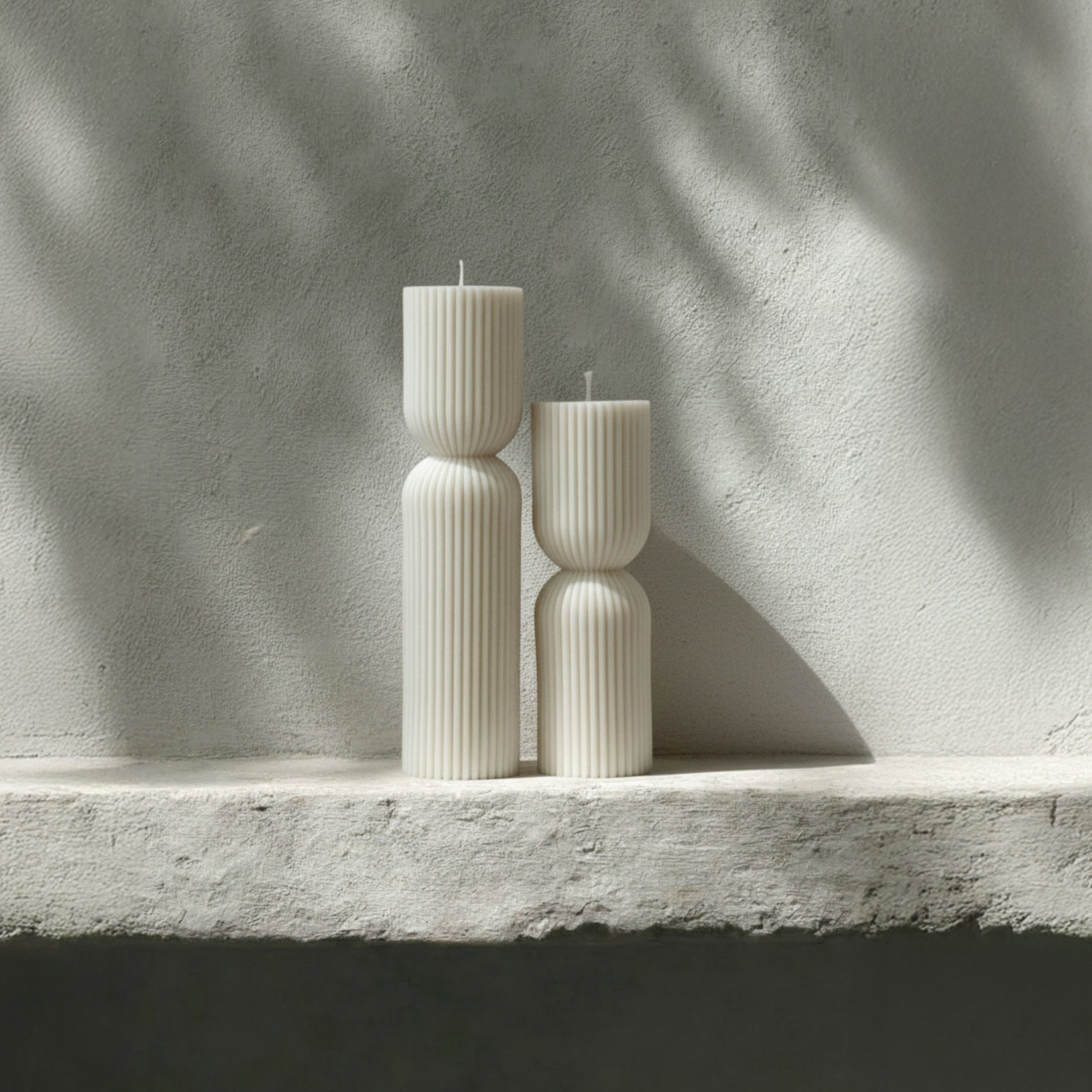 White hourglass set of two candles on a stone surface with a neutral background