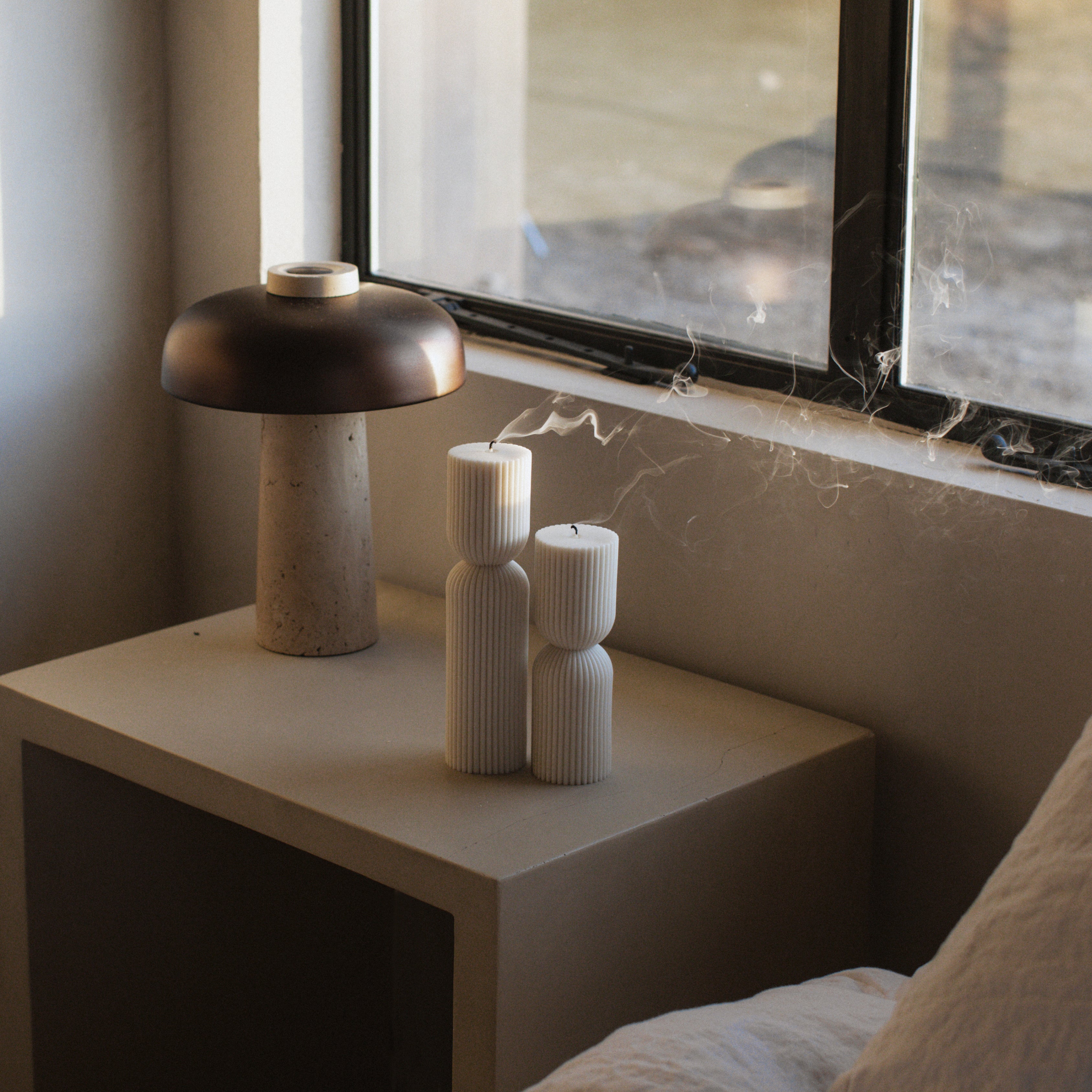 Decorative lamp and white hourglass set of two pillar candles on a nightstand next to a window