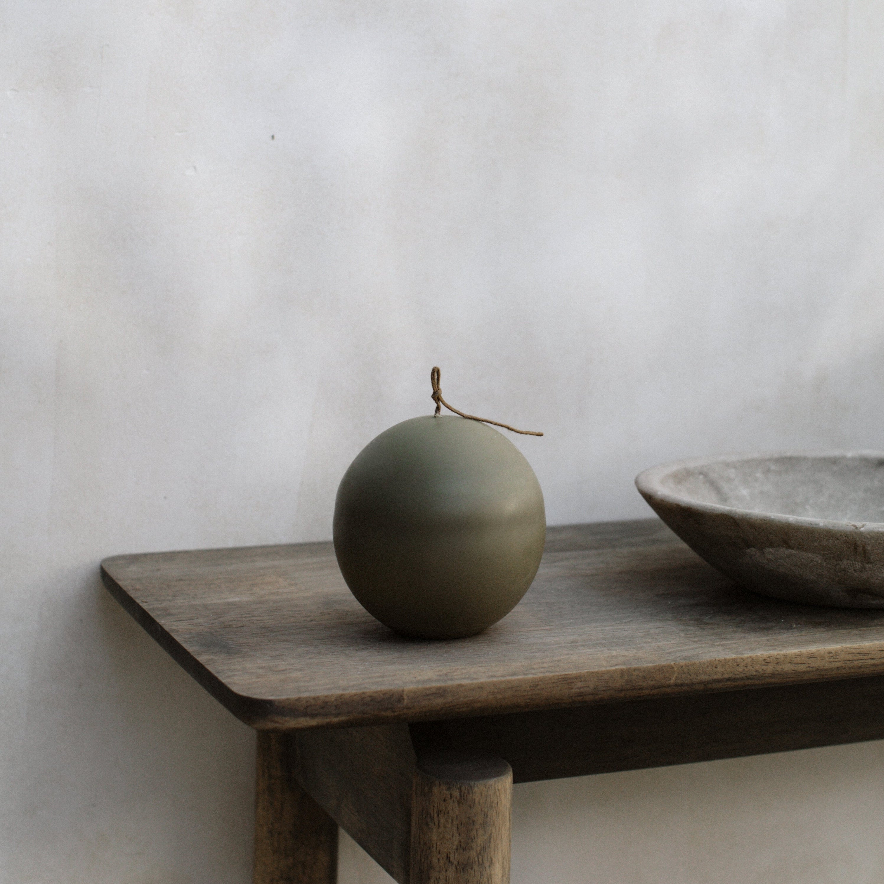 Green imperfect sphere pillar candle on a wooden shelf against a plain wall