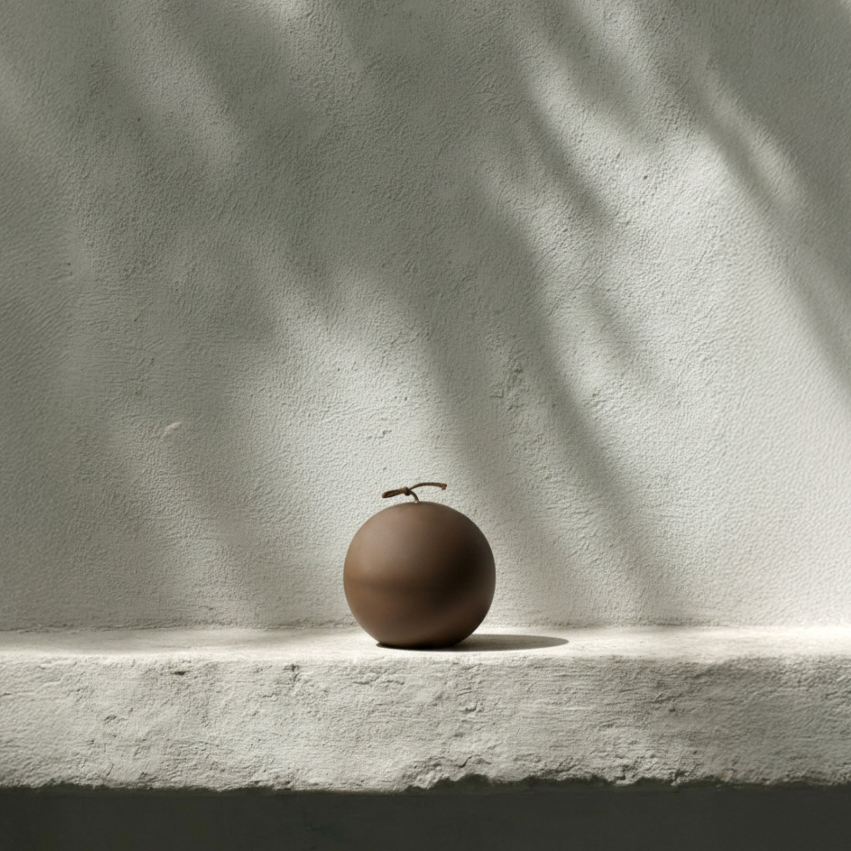 Kobicha brown imperfect sphere pillar candle on a light surface with soft shadows