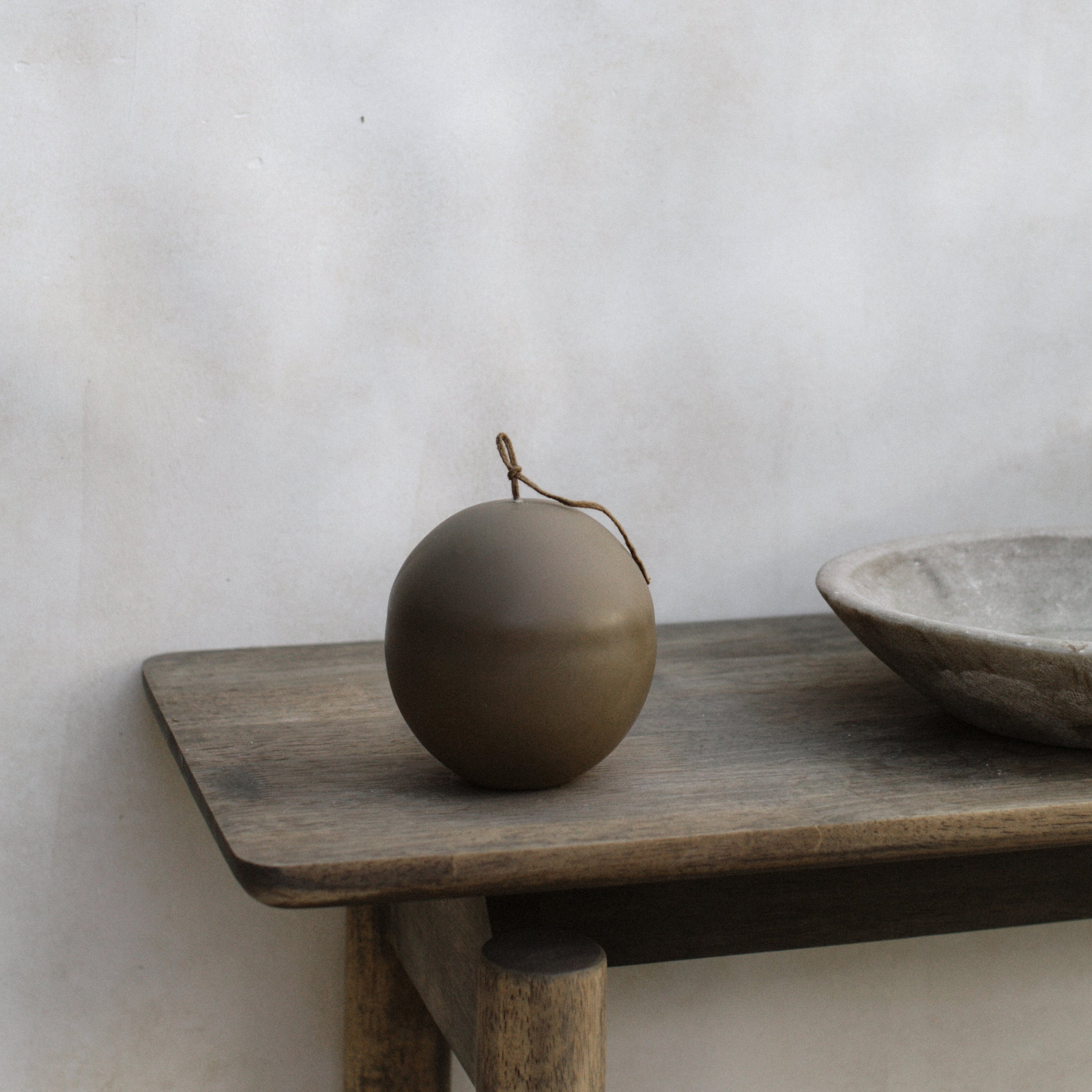 Wooden shelf with an imperfect sphere pillar candle against a plain wall.