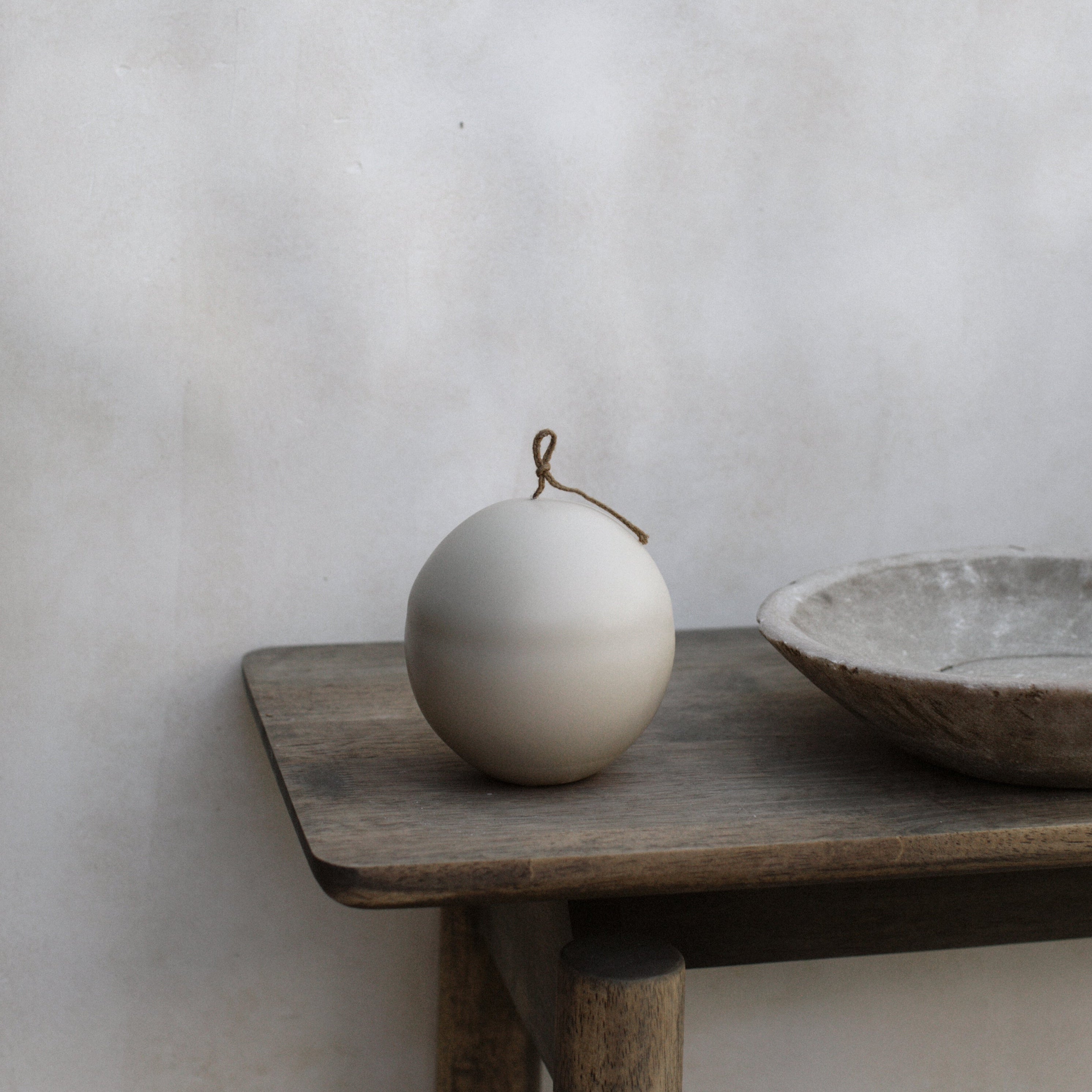 Imperfect light beige sphere pillar candle  on a wooden table against a plain wall.