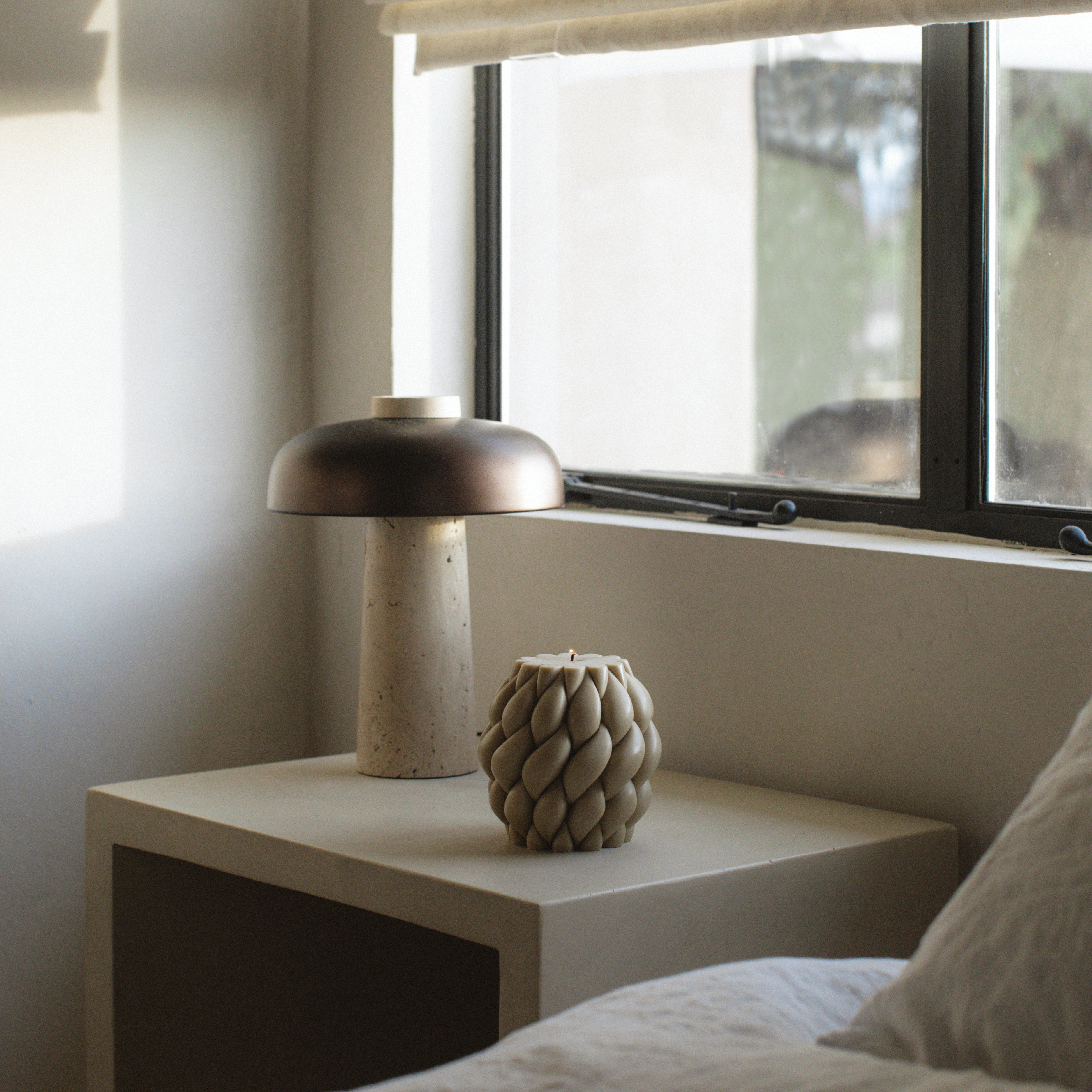 Decorative lamp and olive beige knot ball pillar candle on a nightstand next to a window