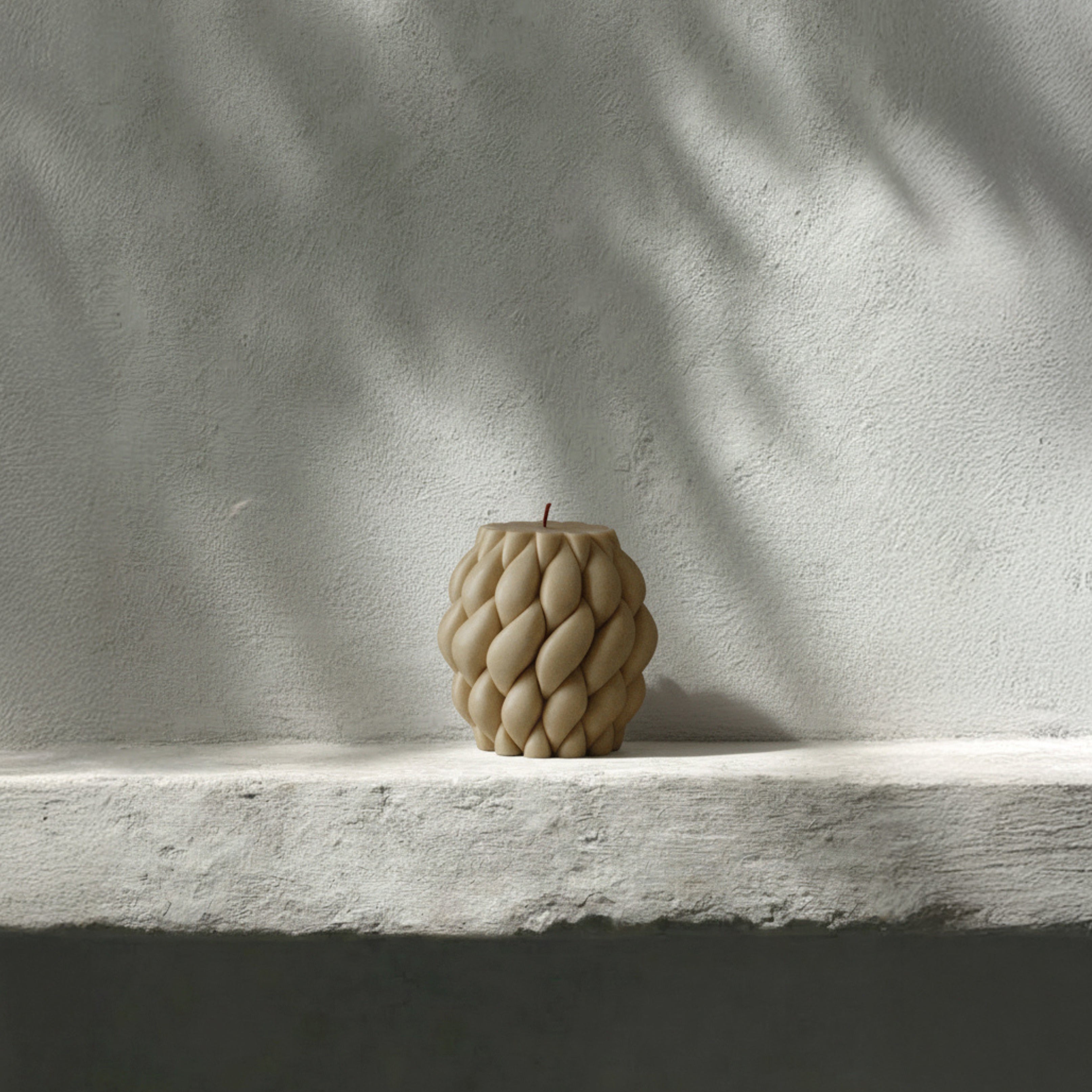 Sandstone knot ball pillar candle on a white shelf with a textured wall background