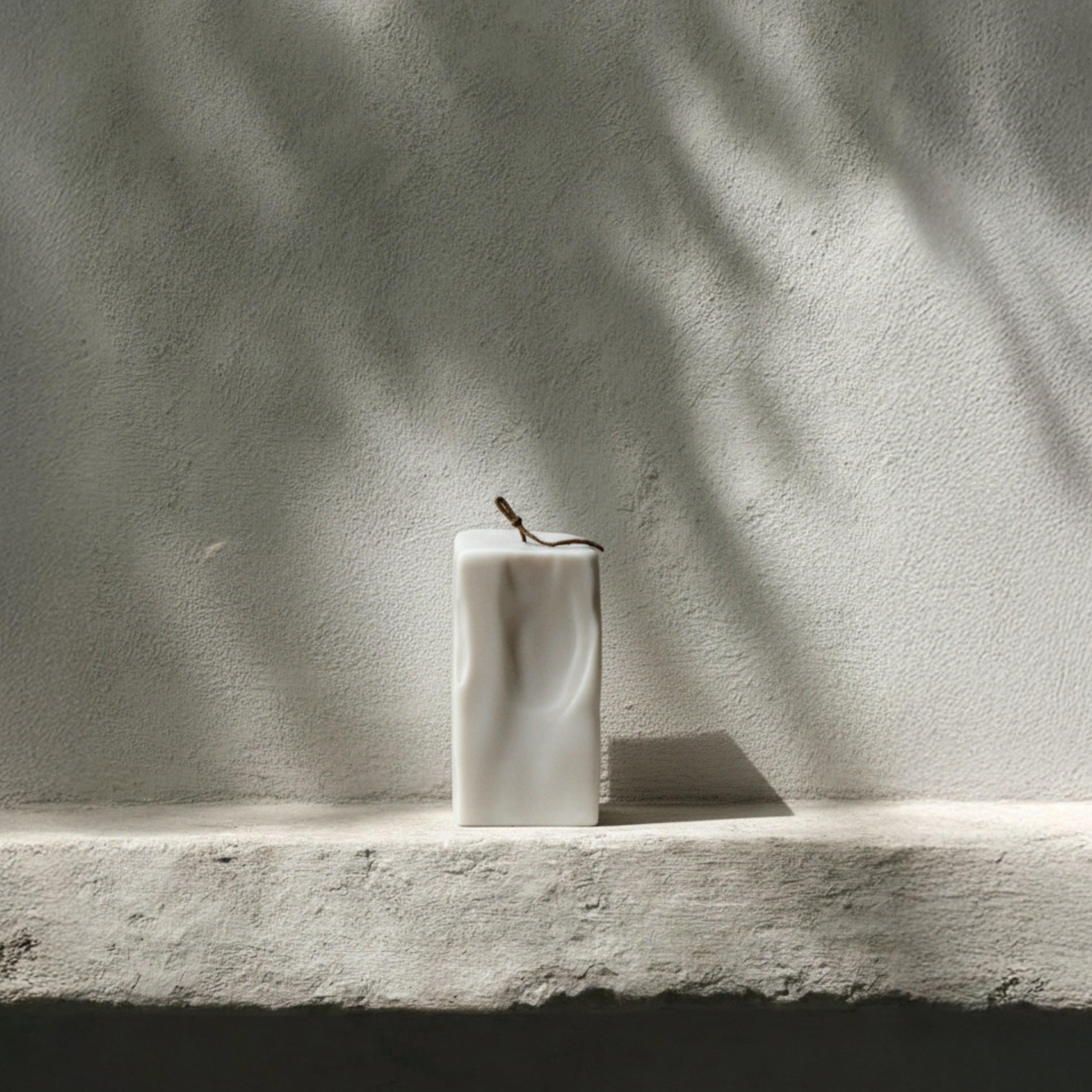 Large raw block pillar candle by LAWA on a stone ledge with a textured wall background