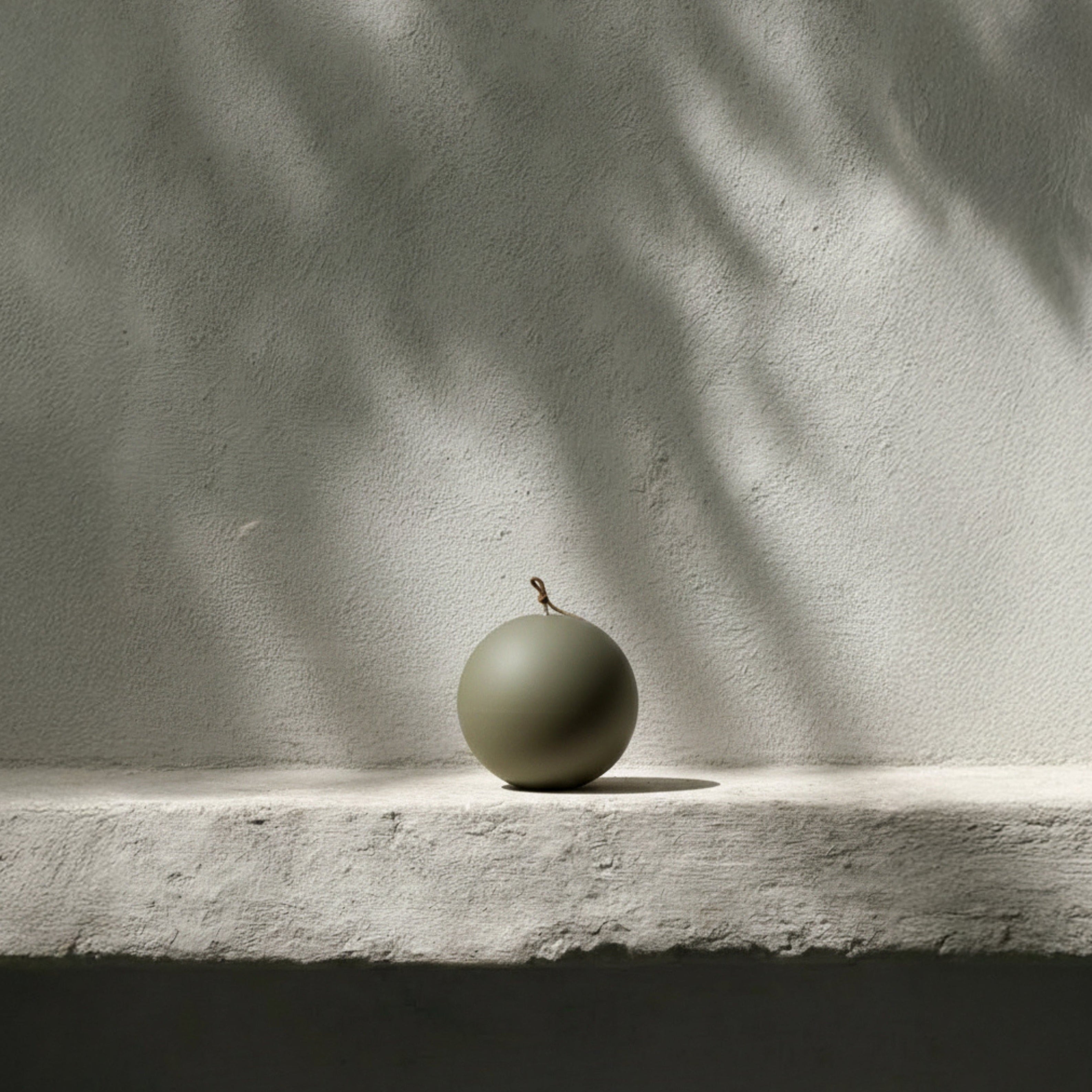 Earthy green sphere candle on a stone surface with a textured wall background