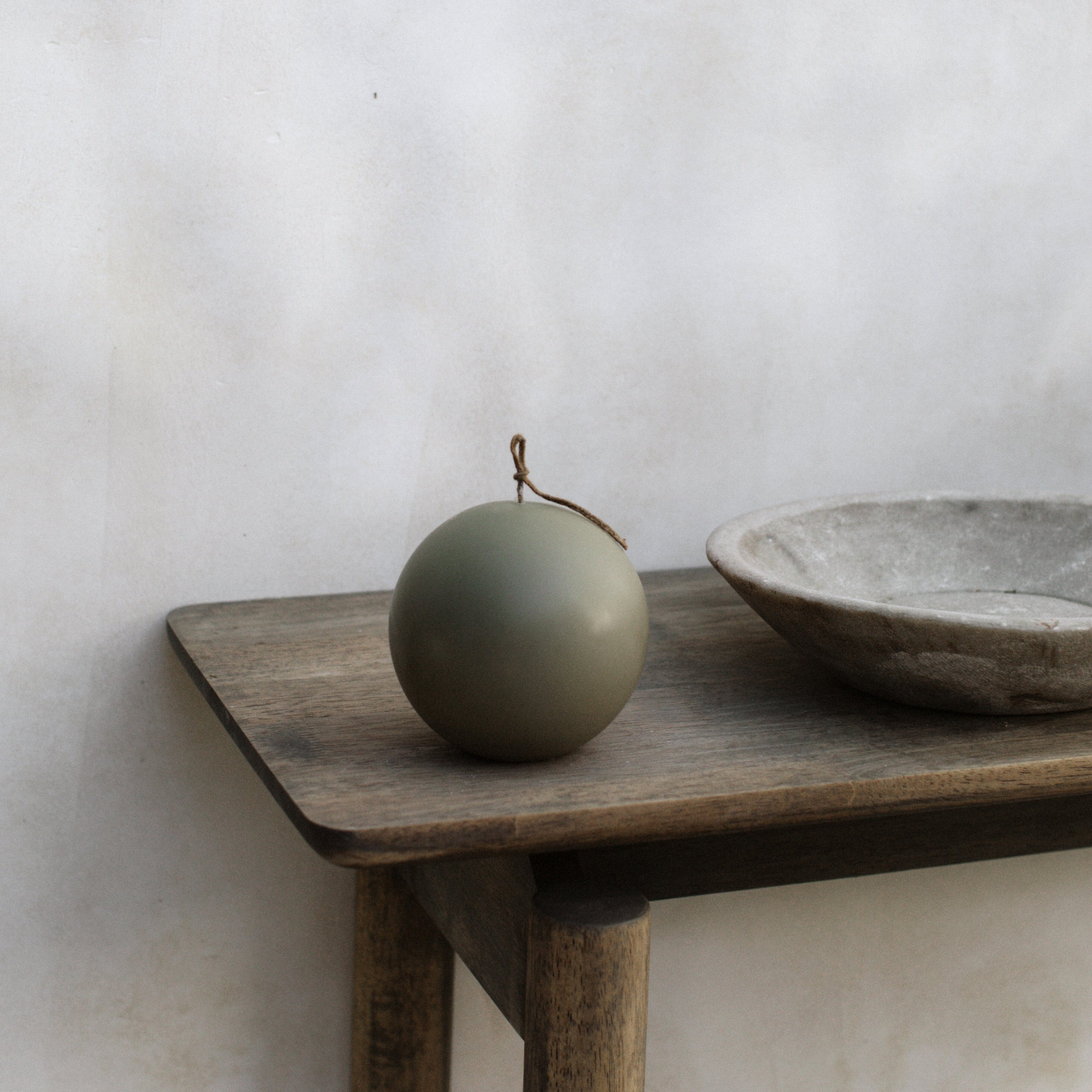 Earthy green sphere pillar candle on a wooden table against a white wall