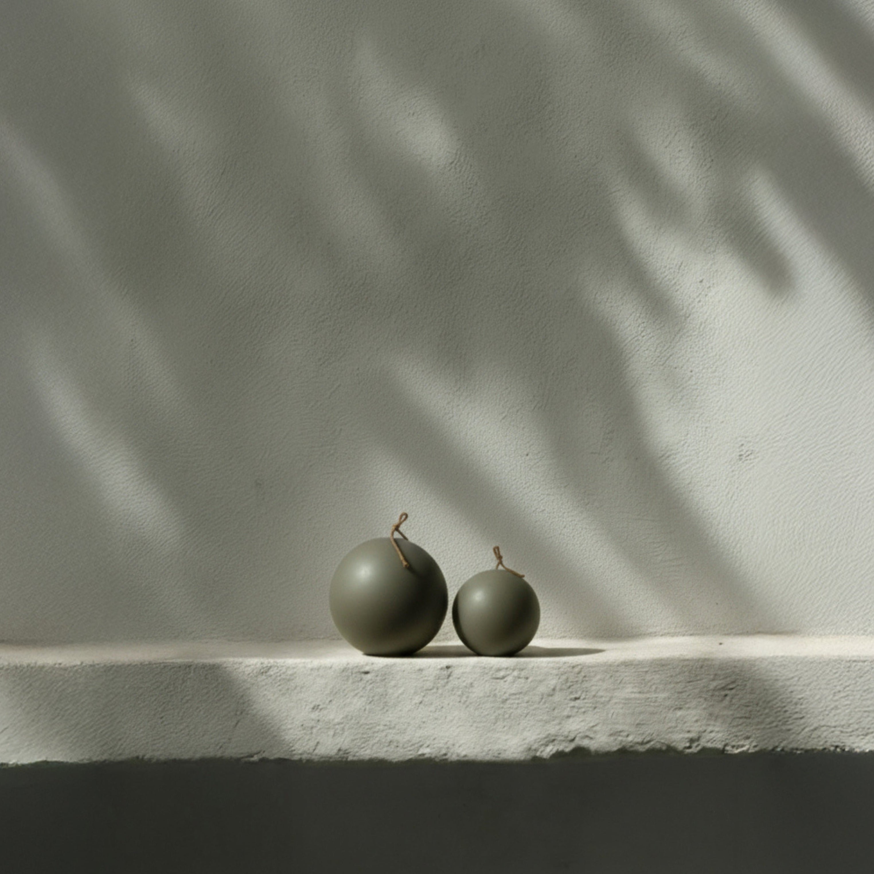 Earthy green sphere candles on a white surface with a shadowy background