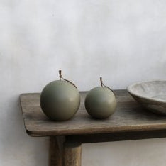 Two green spherical canldes on a wooden surface with a textured wall background