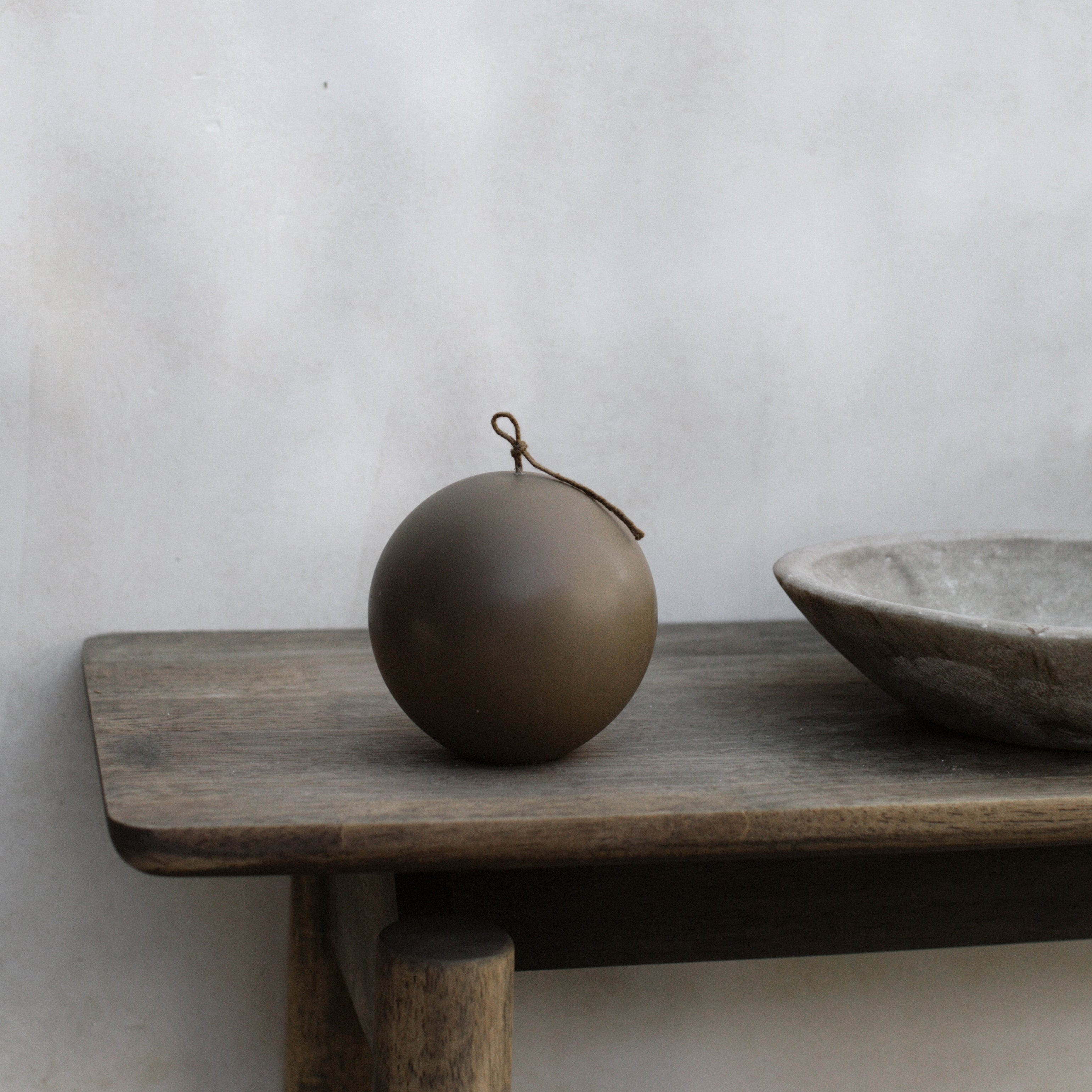 Large kobicha brown pillar candle and bowl on a wooden shelf against a plain wall