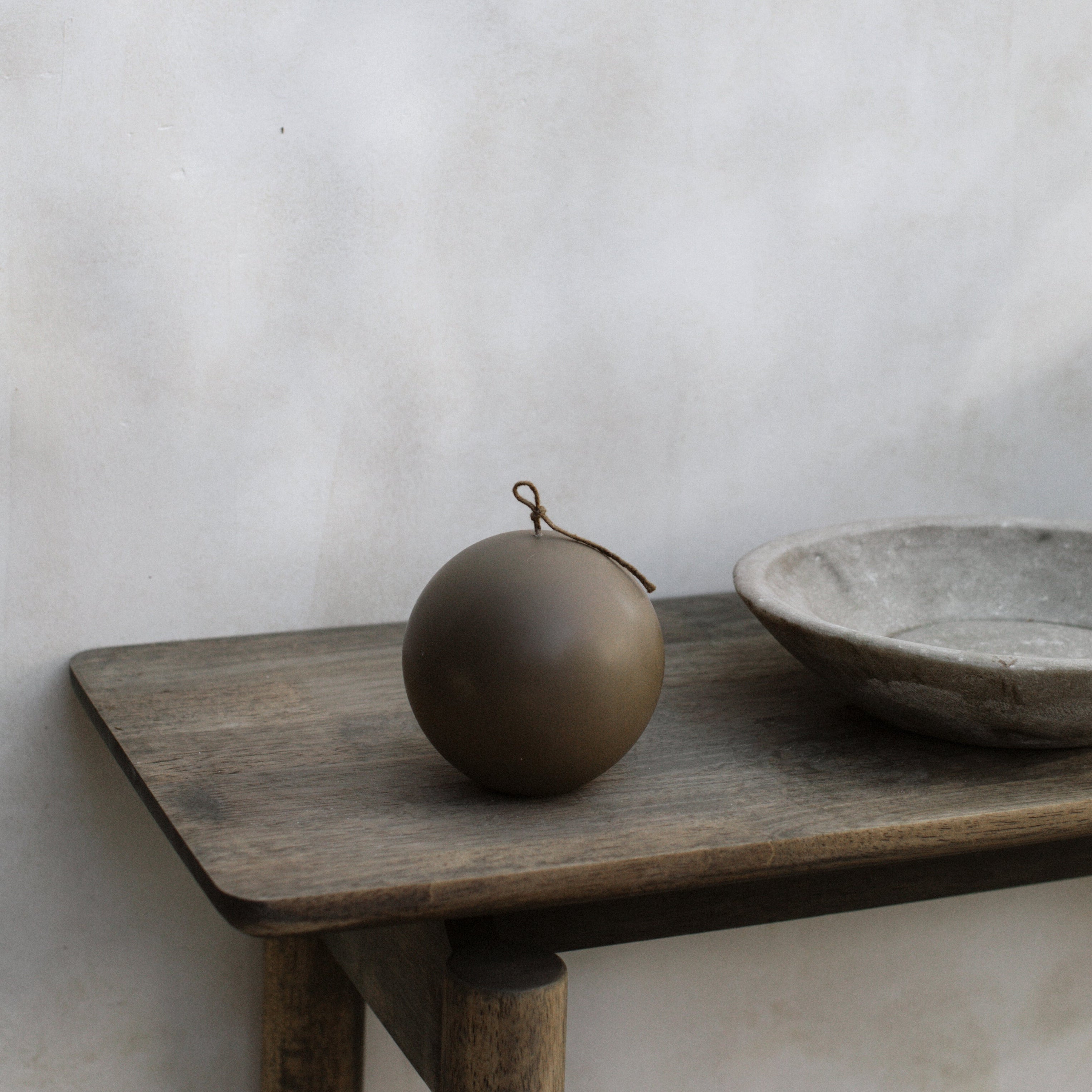 Large kobicha brown pillar  sphere candle on a wooden shelf with a plain background