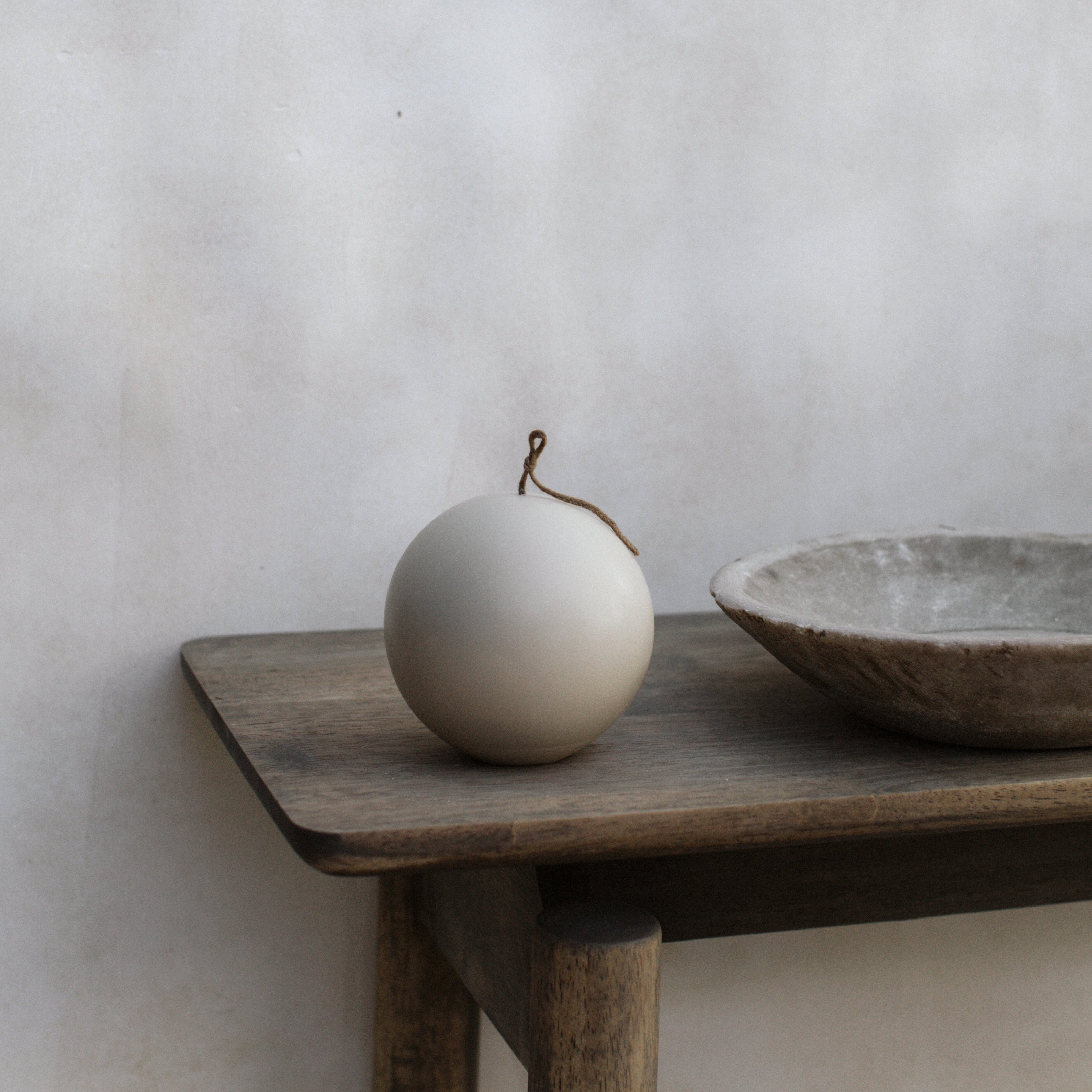 Large light beige sphere pillar candle on a wooden table against a plain wall.