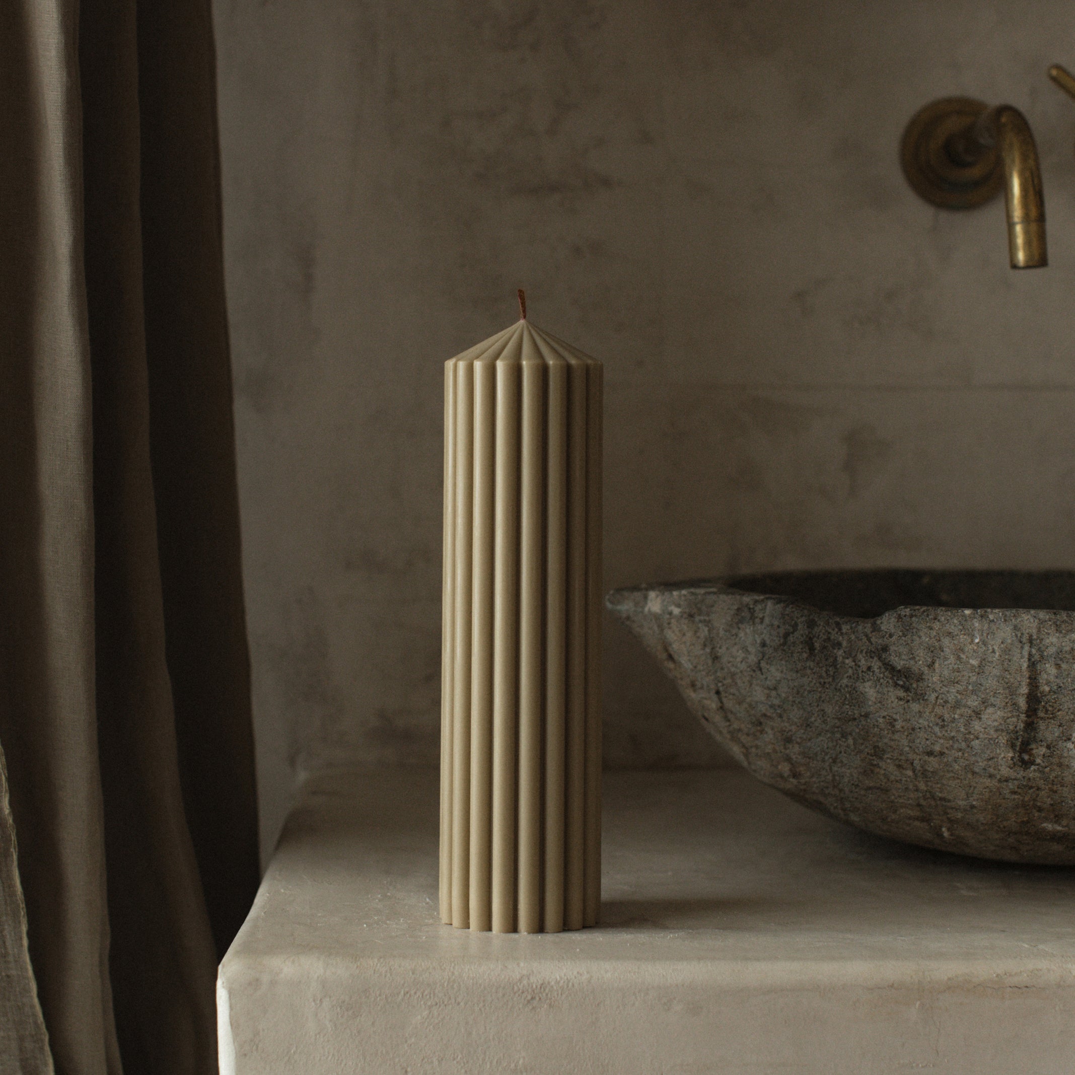 LAWA large olive beige soy wax peak candle featuring bold sculptural geometry on a stone surface with a textured wall and curtain in the background