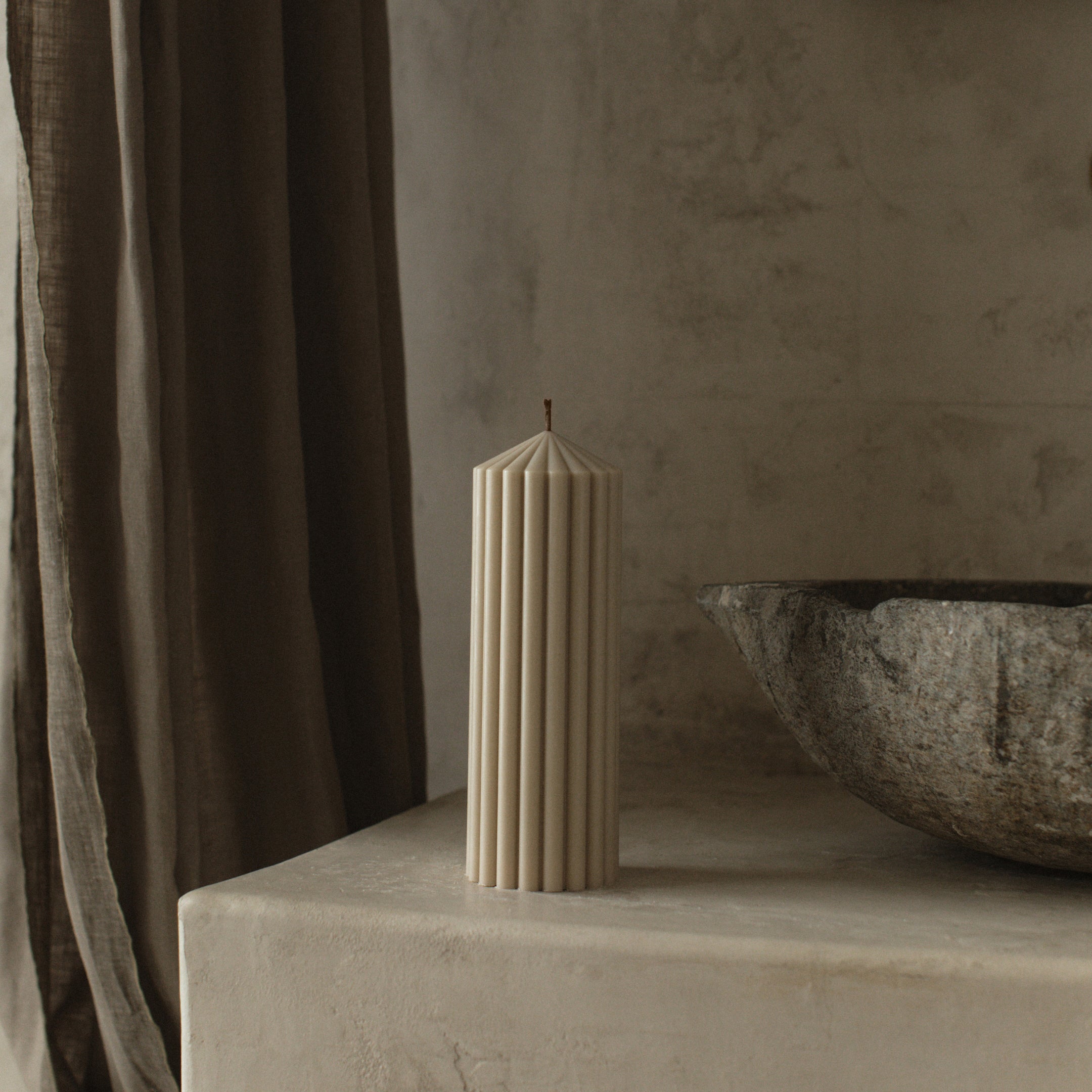 Modern medium moon gray peak candle by LAWA with mountain-like peak form on a stone surface with a textured wall and curtain in the background