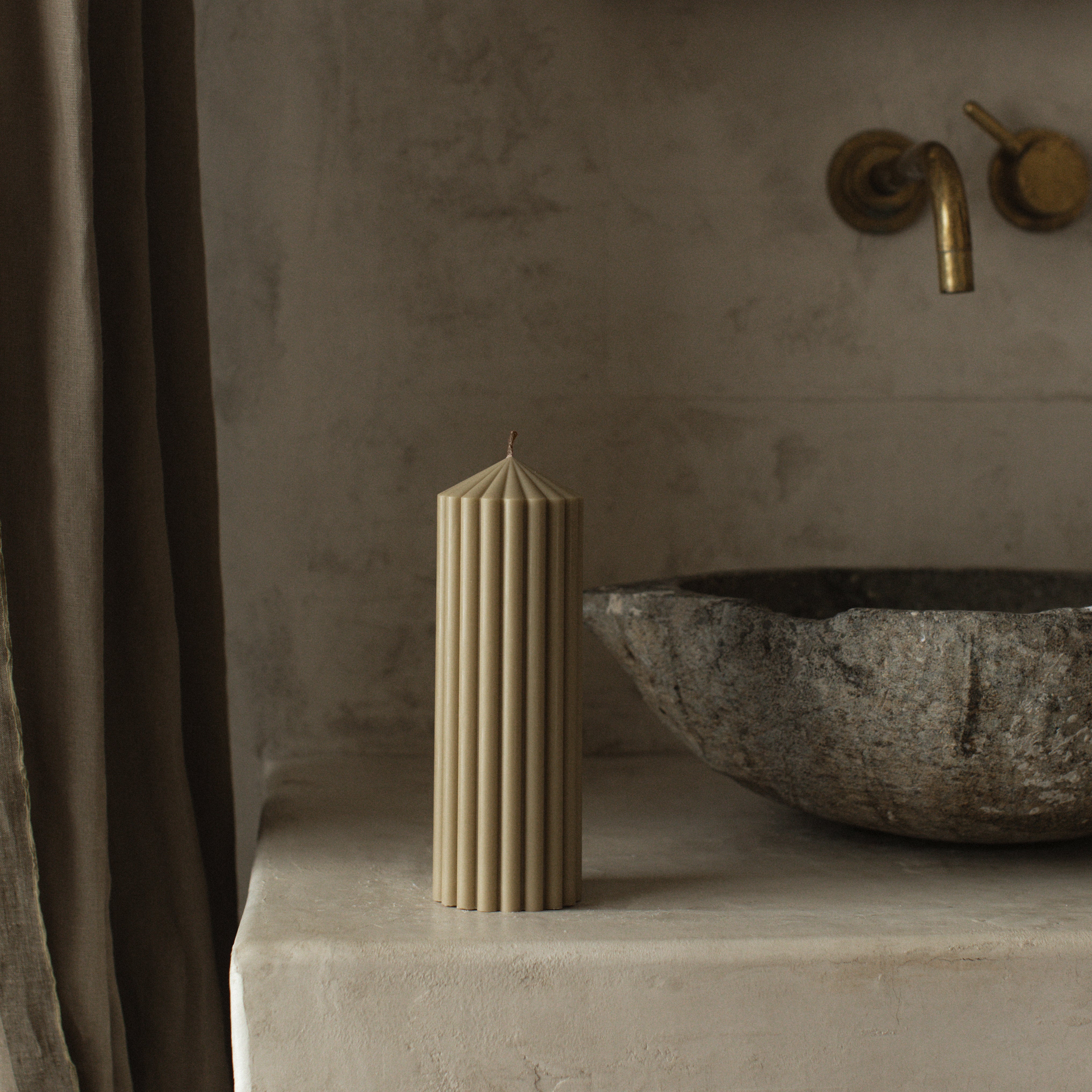 LAWA medium olive beige soy wax candle with modern pointed geometric silhouette on a stone surface with a stone sink.