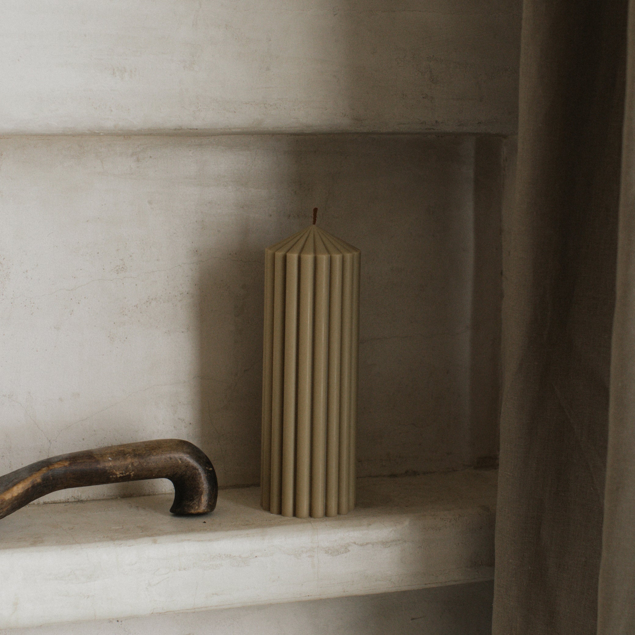 Olive beige medium peak candle by LAWA designed with clean architectural form on a stone shelf with a rustic handle.