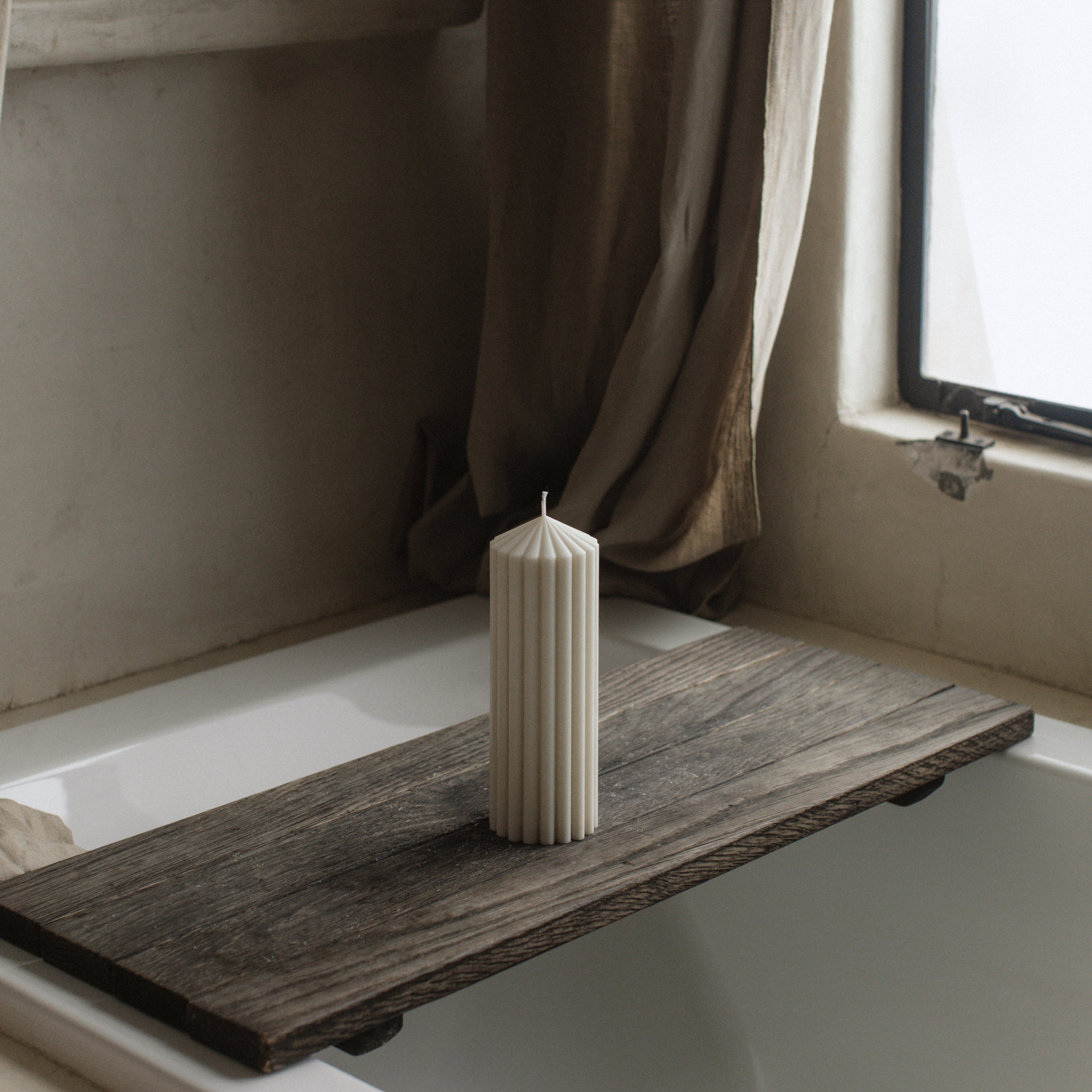 LAWA medium white soy wax peak candle featuring a tall sculptural silhouette on a wooden shelf in a bathroom with a bathtub and window.