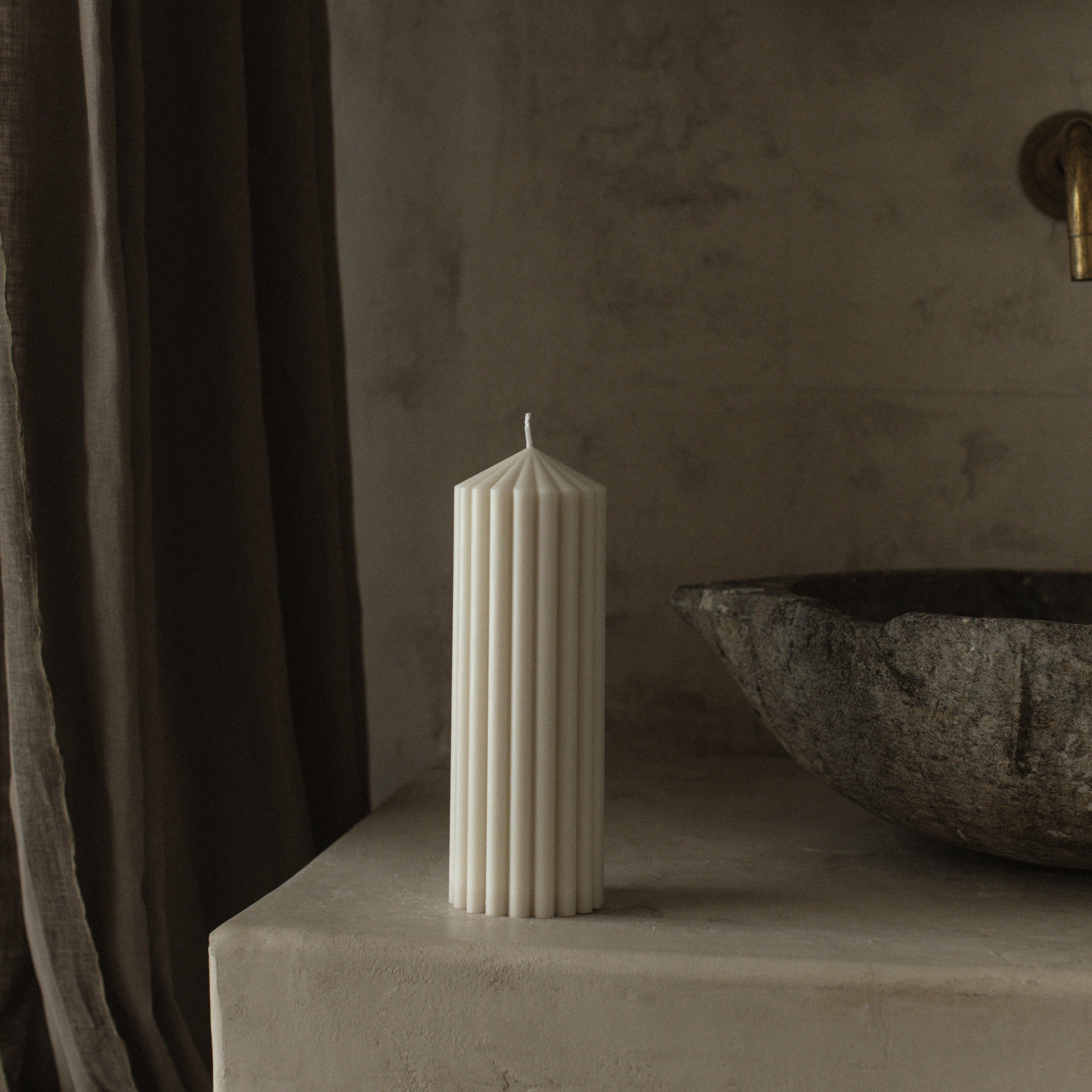 White medium peak candle by LAWA with a clean geometric mountain shape on a stone surface with a stone bowl and dark curtain in the background