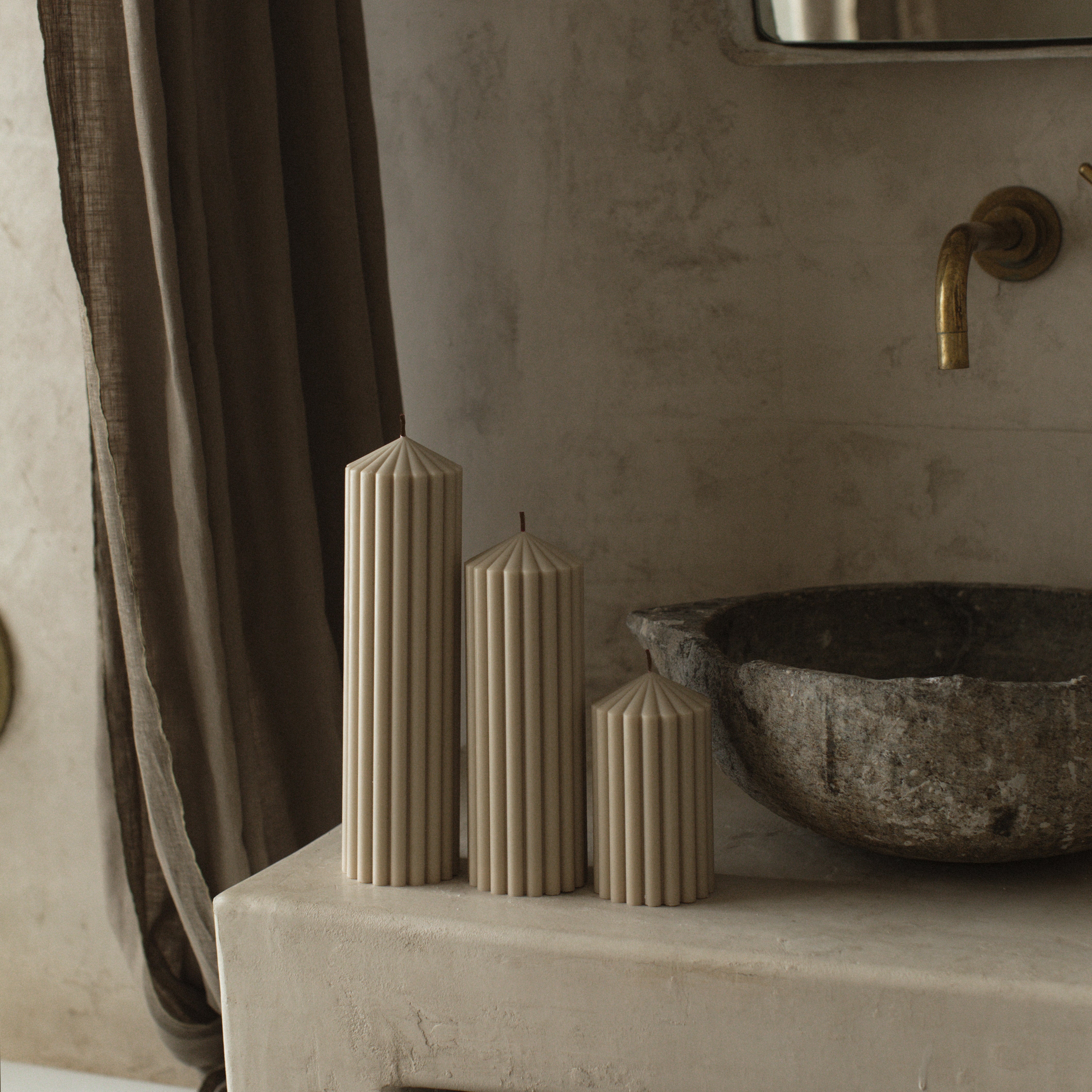 LAWA moon gray peak candle trio with sculptural mountain-inspired shapes on a surface with a stone sink and faucet in the background