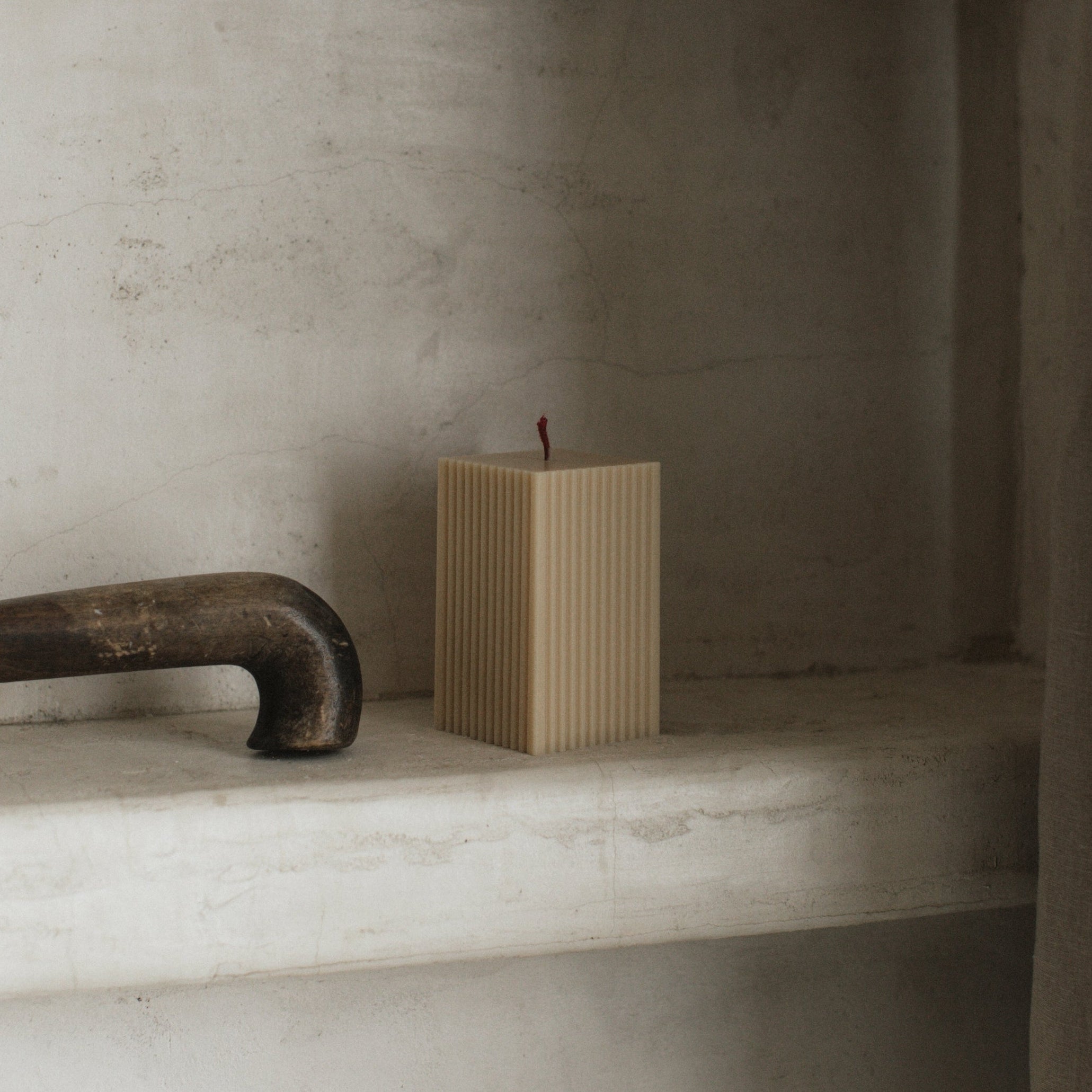 Sandstone ribbed square candle by LAWA with structured soy wax design on a stone shelf in the bathroom